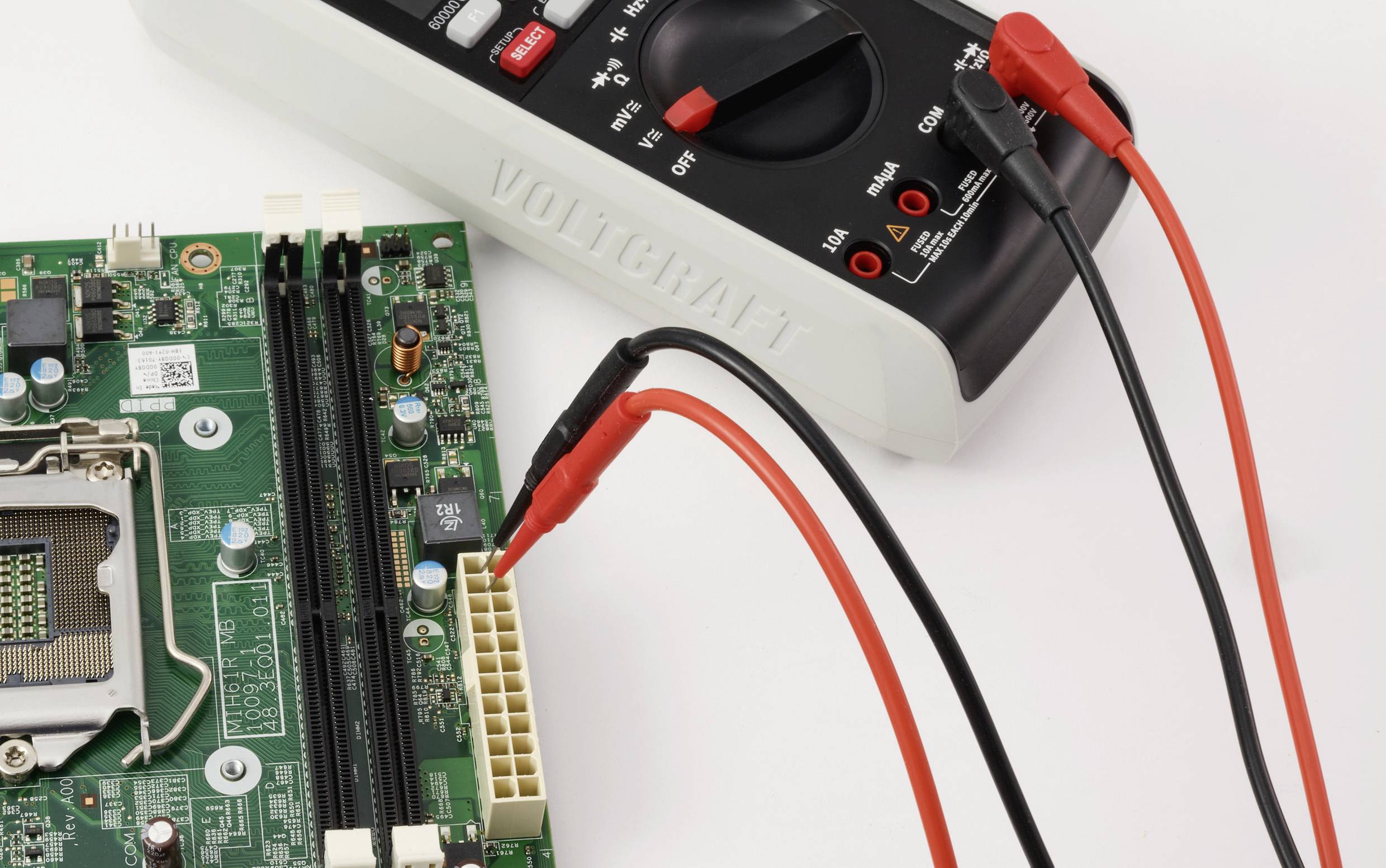 Multimetr s červenými a černými sondami testuje připojení na počítačové základní desce, což indikuje elektronickou diagnostiku nebo opravárenské práce.