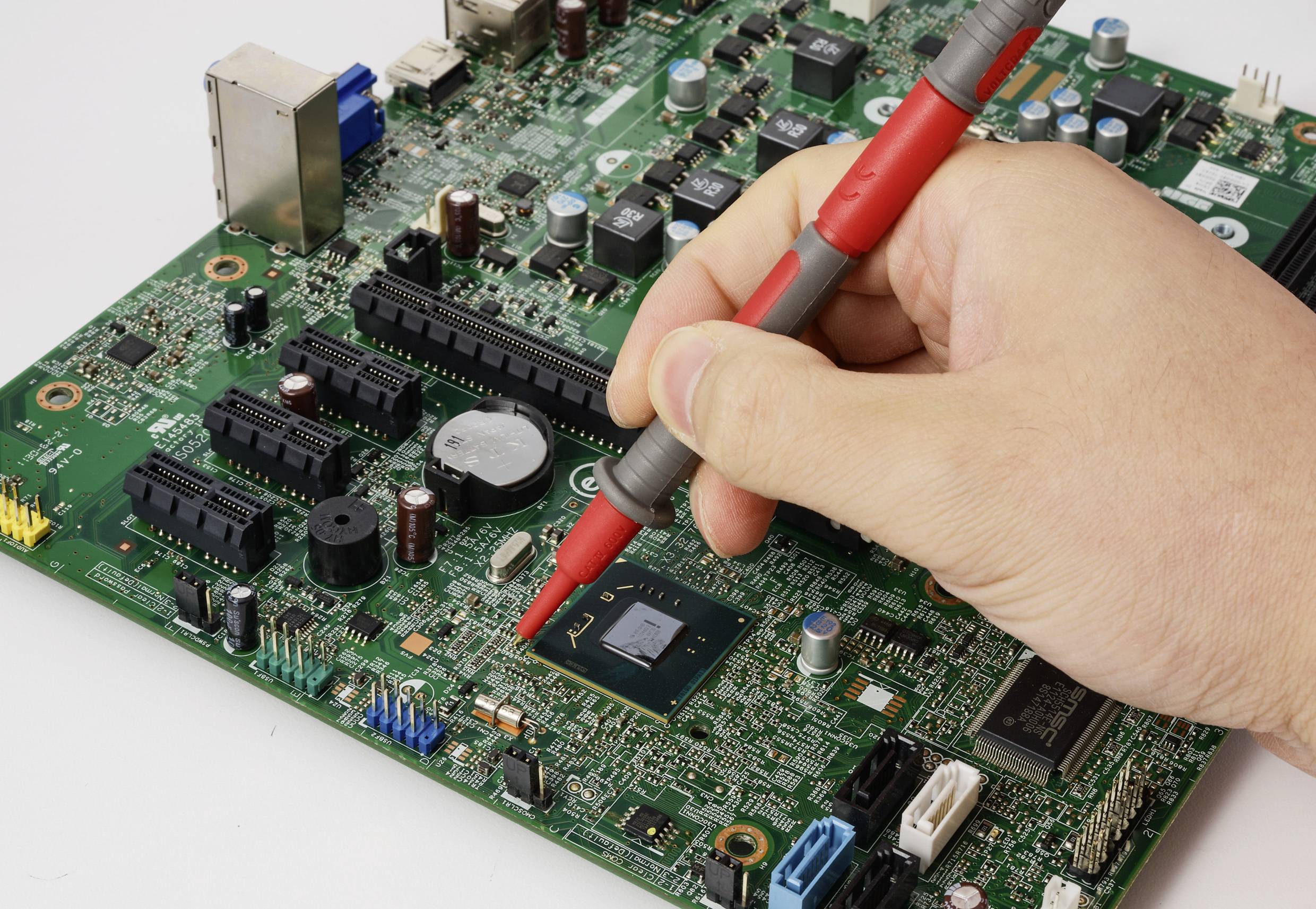 Ruka používá červenou sondu na základní desce počítače a testuje elektronické komponenty.
