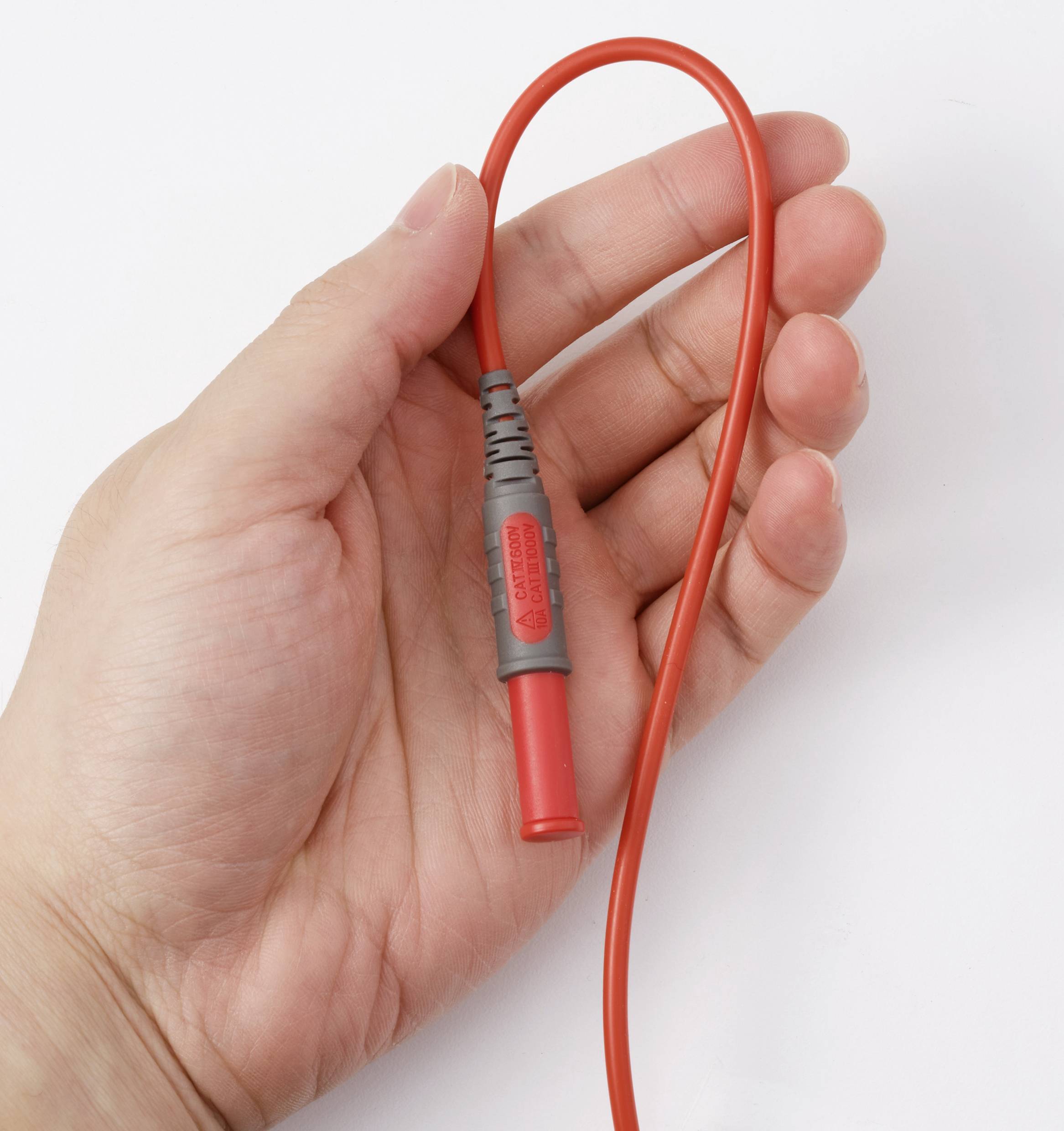 Ruka držící červenou elektrickou sondu s flexibilním vodičem, používaná pro testování elektrických obvodů.