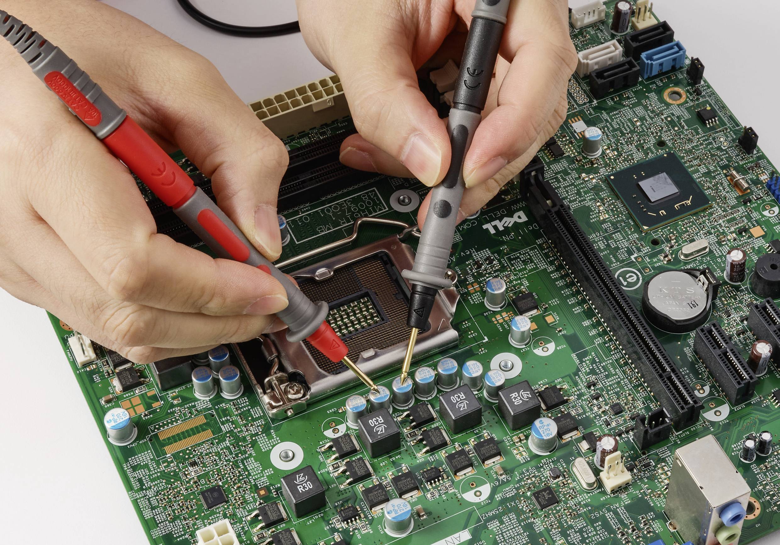 Ruce používající sondy pro testování a kontrolu elektronické desky plošných spojů s různými komponenty, ilustrující elektronickou práci.