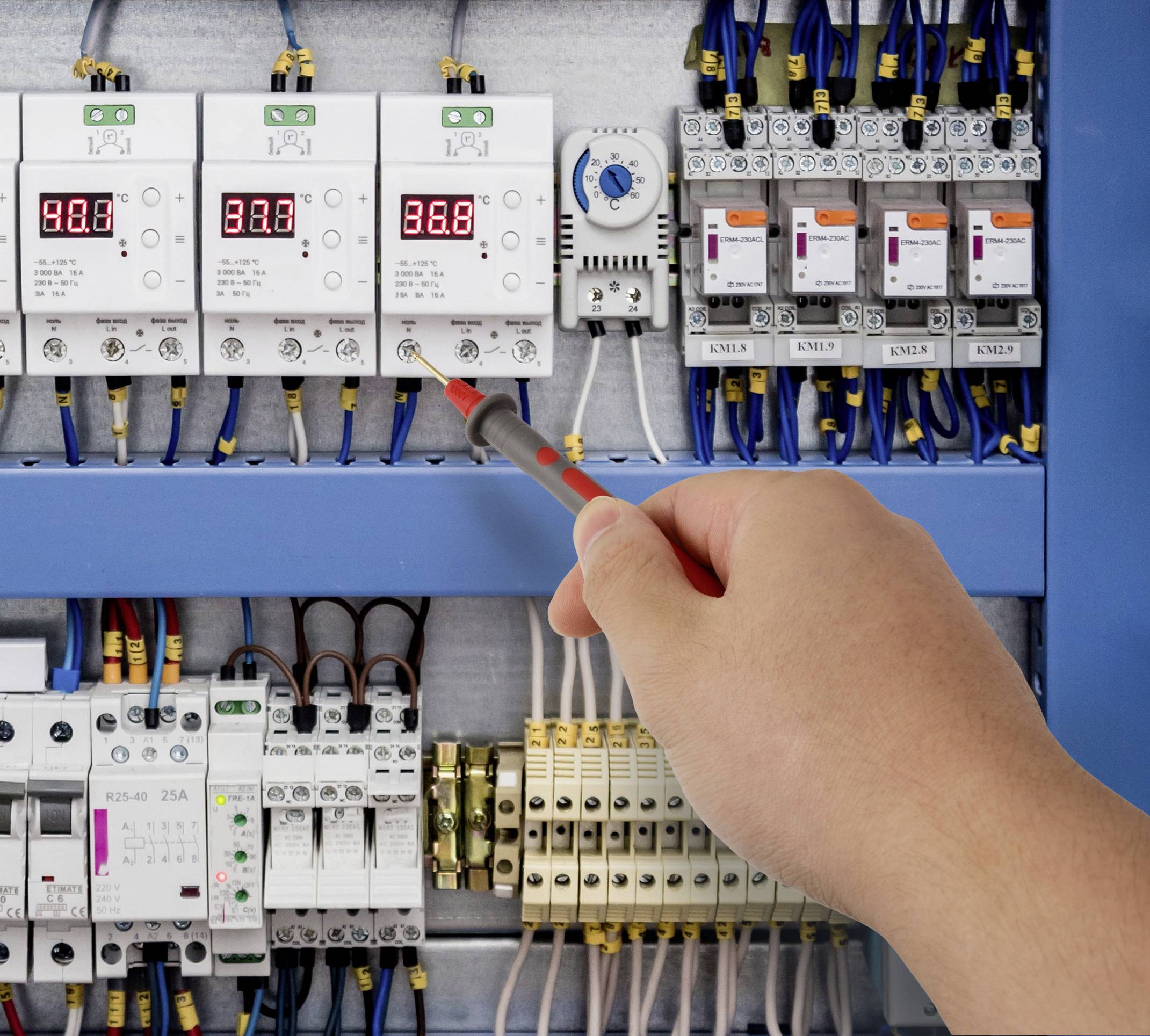 Elektrikář používá šroubovák k nastavení parametrů na elektrickém rozvaděči s digitálními měřicími přístroji zobrazujícími napětí a přepínači.