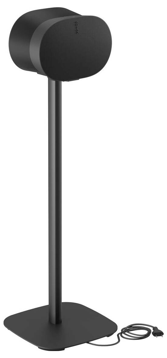 Černý reproduktor na podlahu s kruhovým podstavcem a dlouhou nohou, vyznačující se minimalistickým designem a viditelným napájecím kabelem ležícím na podlaze.