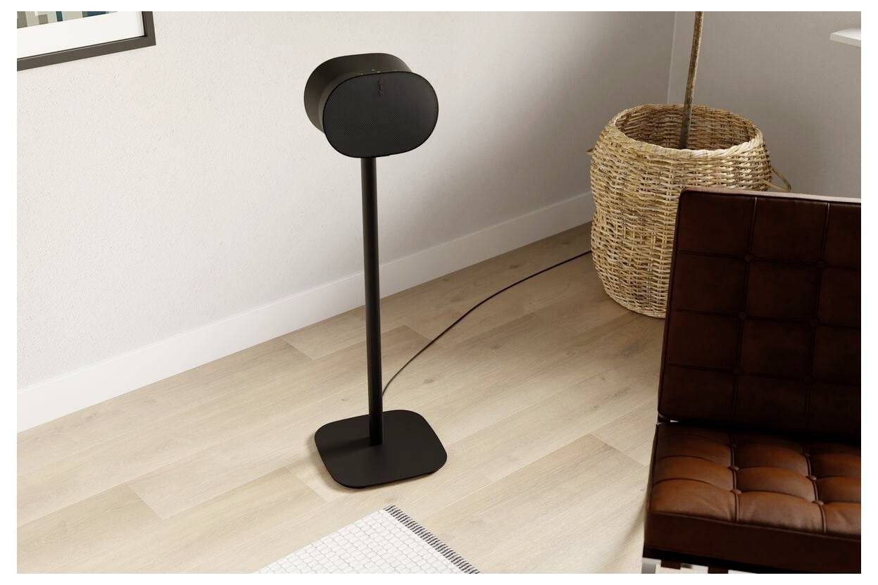 Moderní černá stojací lampa na dřevěné podlaze vedle tkané košíku a hnědé kožené židle v minimalistickém pokojovém prostoru.