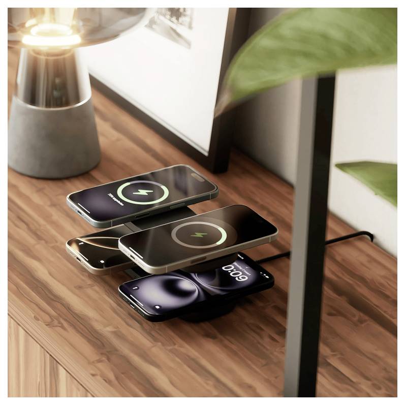 Dřevěný stůl drží bezdrátovou nabíjecí podložku se čtyřmi navrstvenými mobilními telefony, které zobrazují nabíjecí ikony, vedle lampy a rostliny.