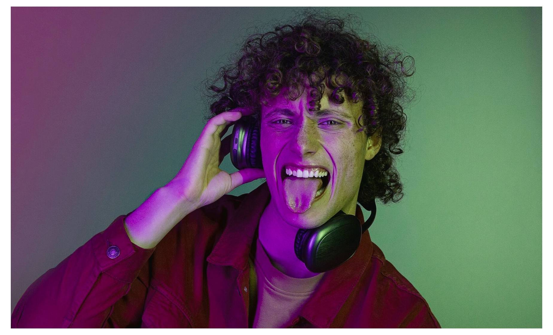 Osoba s nasazenými sluchátky dělá hravý výraz vypláznutím jazyka na barevném pozadí.