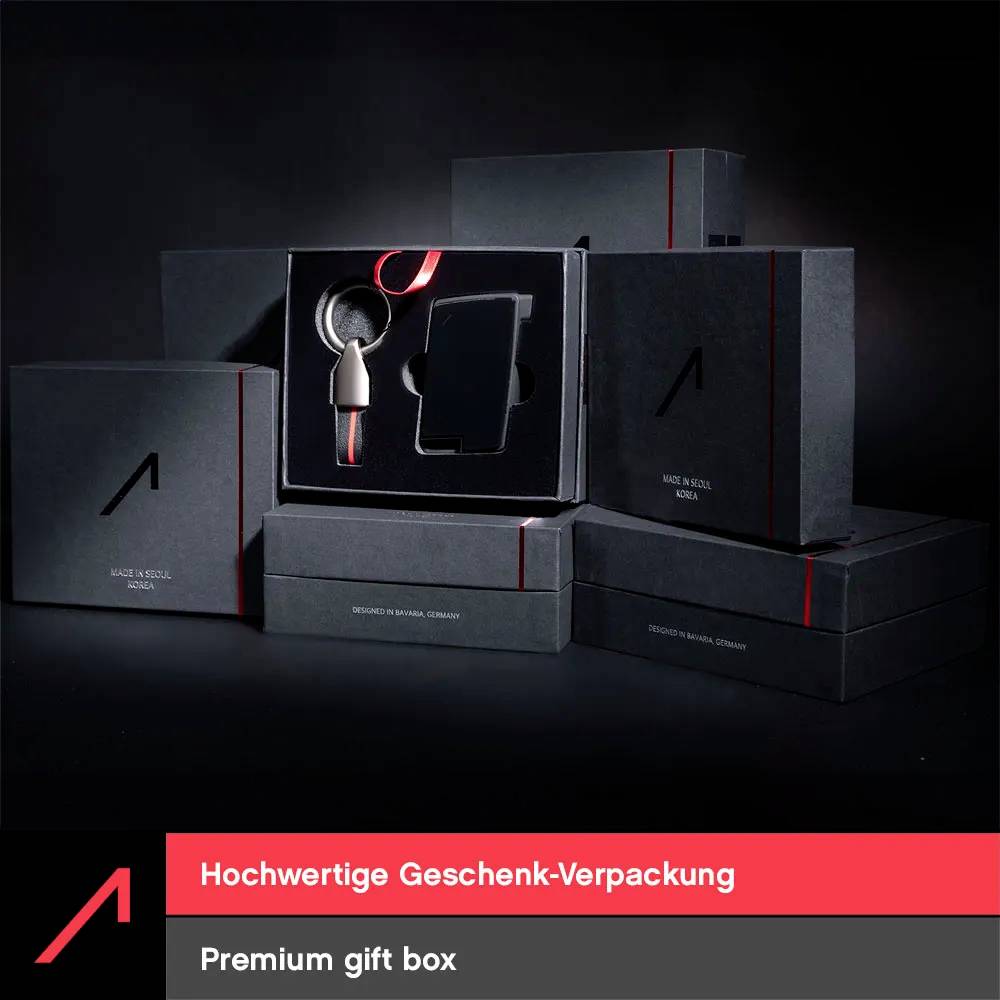 Sada "prémiový dárkový box" zobrazená v černém obalu s červenými akcenty, prezentující přívěsek na klíče a obal na smartphone.