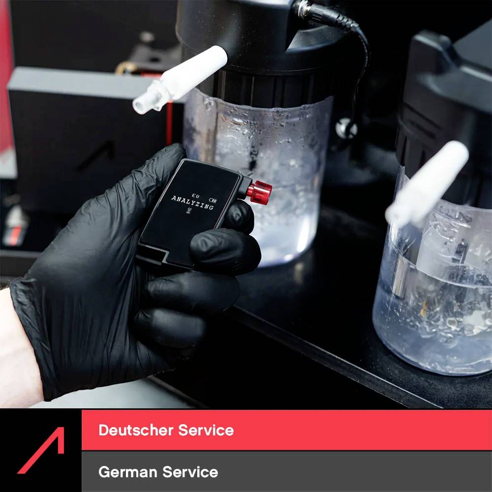 Ruka v černé rukavici drží malou nádobku označenou "Deutscher Service, Německý servis" poblíž dvou větších laboratorních nádob.