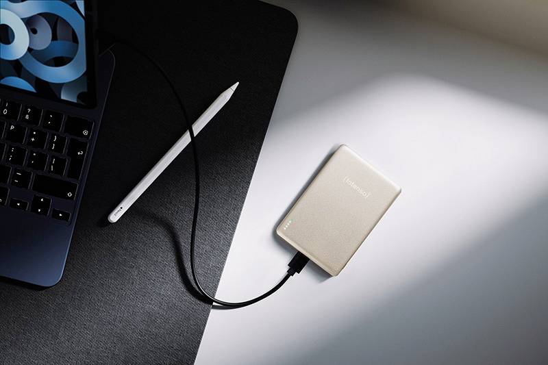 Stříbrný externí pevný disk připojený k notebooku na stole, vedle něj stylus.