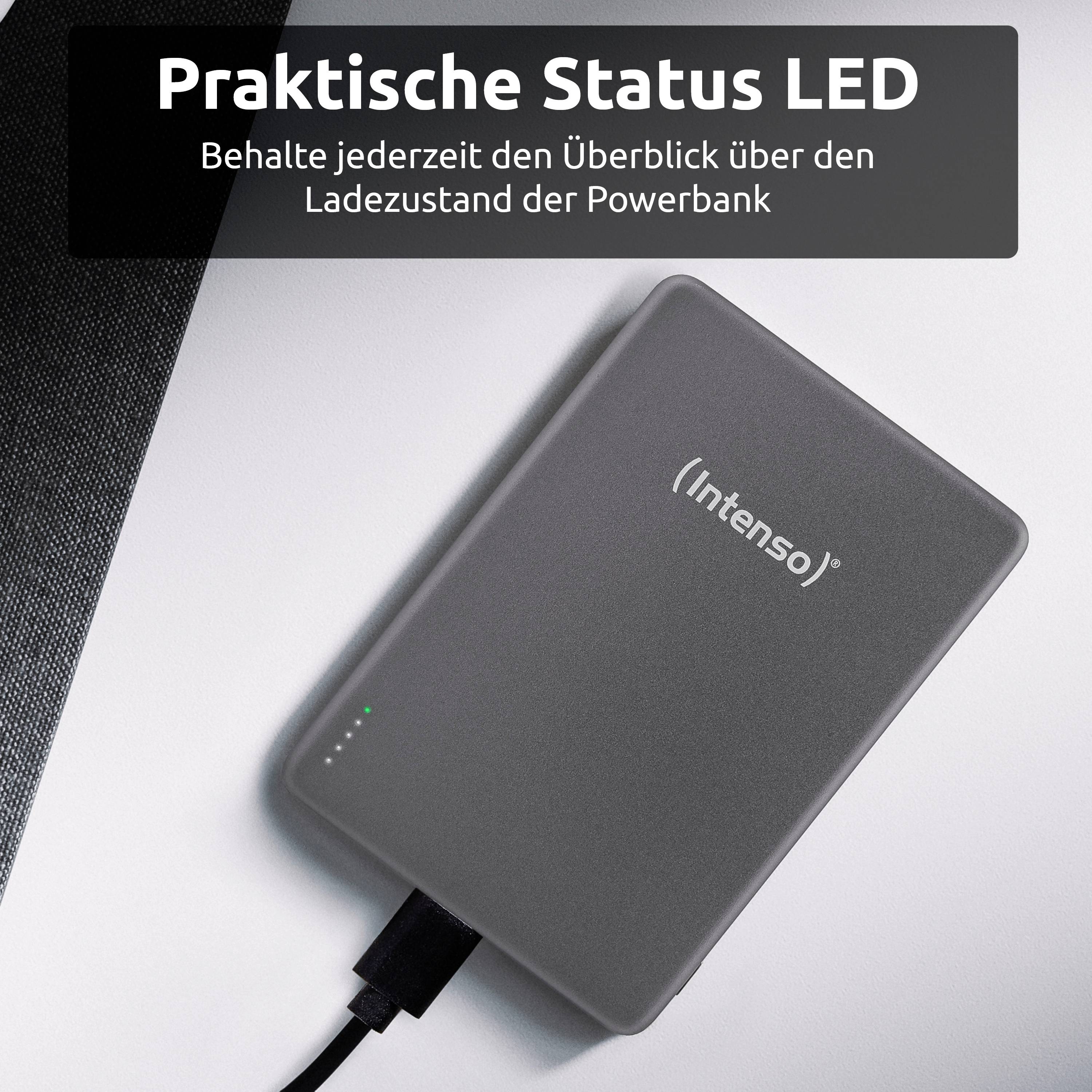 Šedá powerbanka Intenso s indikátorem LED stavu nabití se nabíjí a leží na bílém povrchu. Text v němčině zmiňuje sledování stavu nabití.