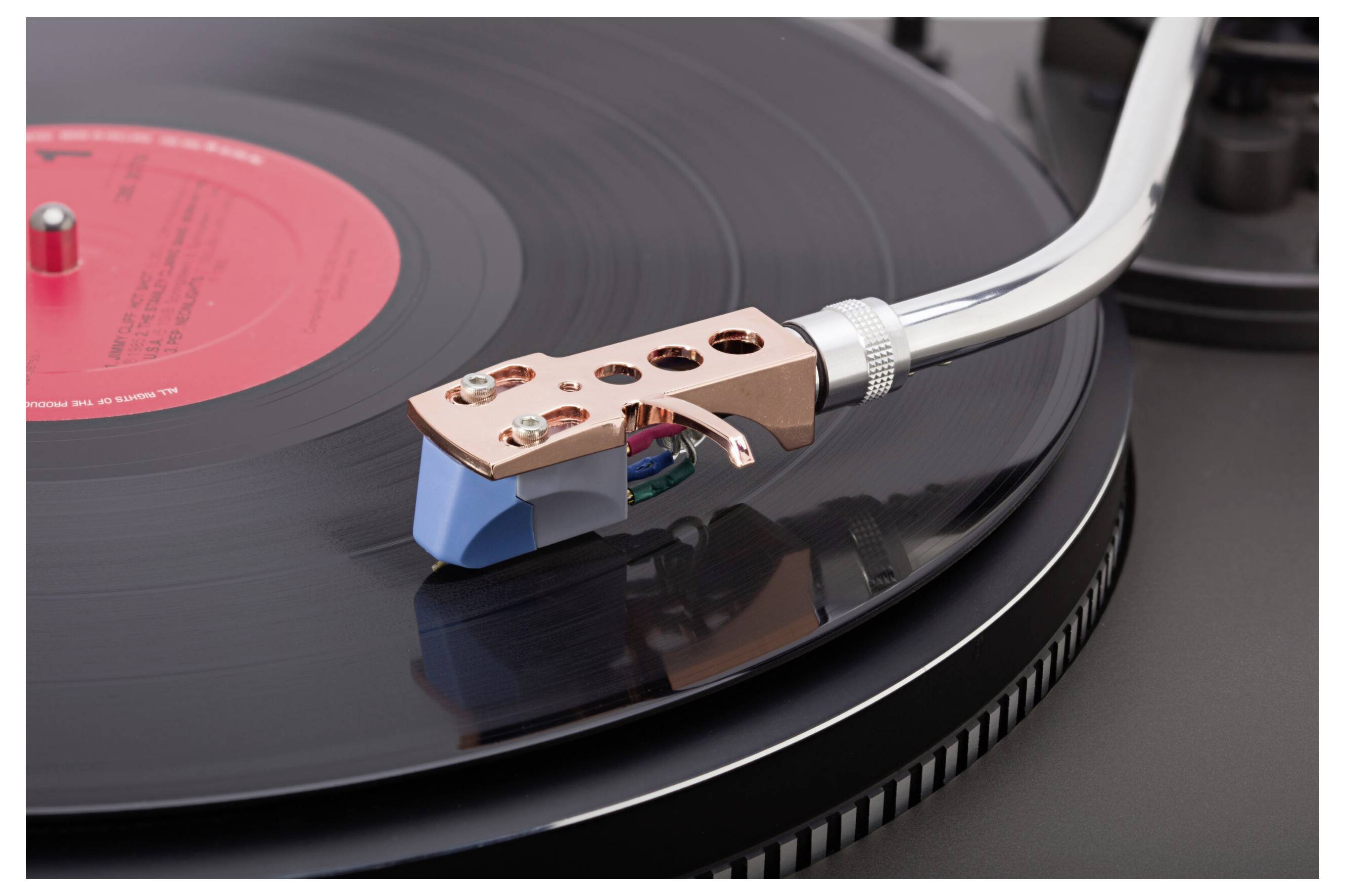 Detailní záběr jehly gramofonu na černé vinylové desce, který odhaluje jemné detaily tonearmu a přenosky.