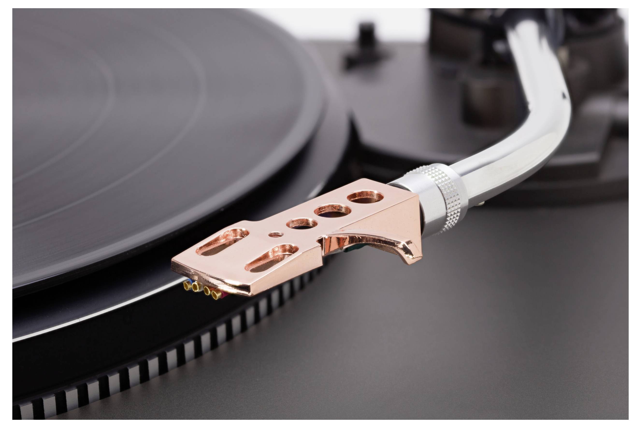 Detailní záběr ramene gramofonu a stylů umístěných nad vinylovou deskou, který zdůrazňuje přesnost jehly a drážek.
