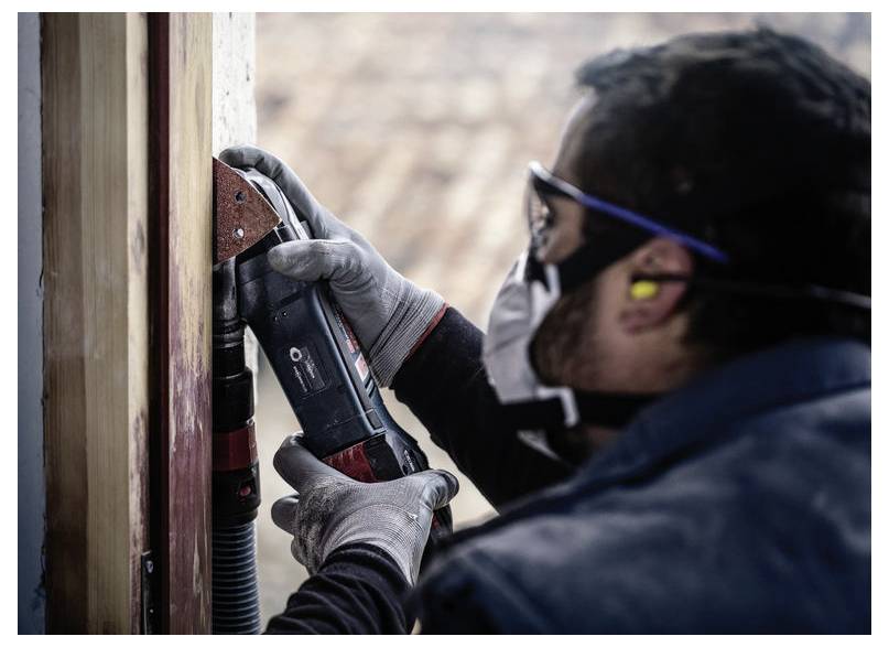 Dělník v ochranném oblečení používá elektrické nářadí na dřevěném povrchu.