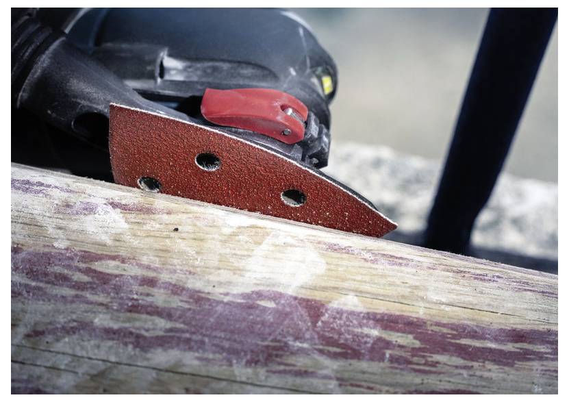 Elektrická bruska s červeným brusným kotoučem hladí kus dřeva, odstraňuje starou barvu a odhaluje přirozené dřevní vlákno pod ní.
