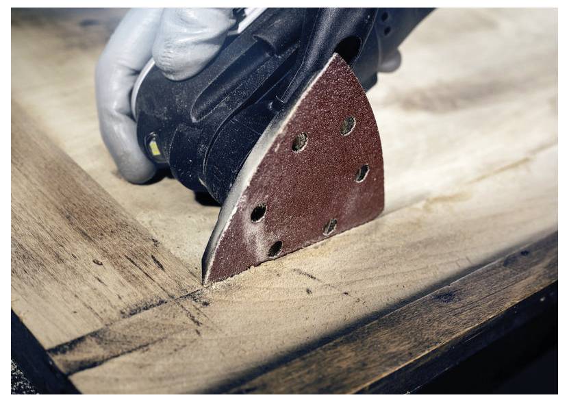 Osoba používá ruční elektrickou brusku na rohu dřevěného povrchu, který vyhlazuje červeným brusným kotoučem.