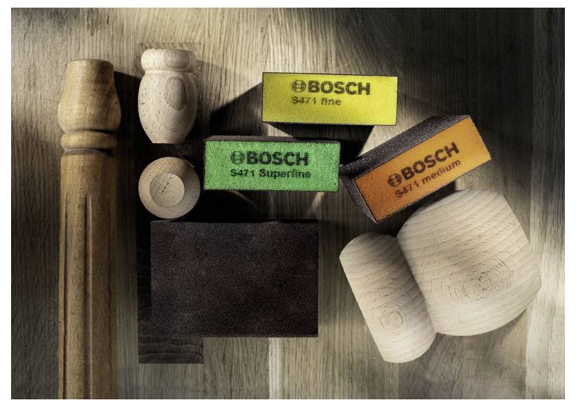 Brusné podložky označené "Bosch S471 hrubé, velmi jemné, střední" s otočenými dřevěnými předměty na dřevěném povrchu, zvýrazňující truhlářské nástroje.