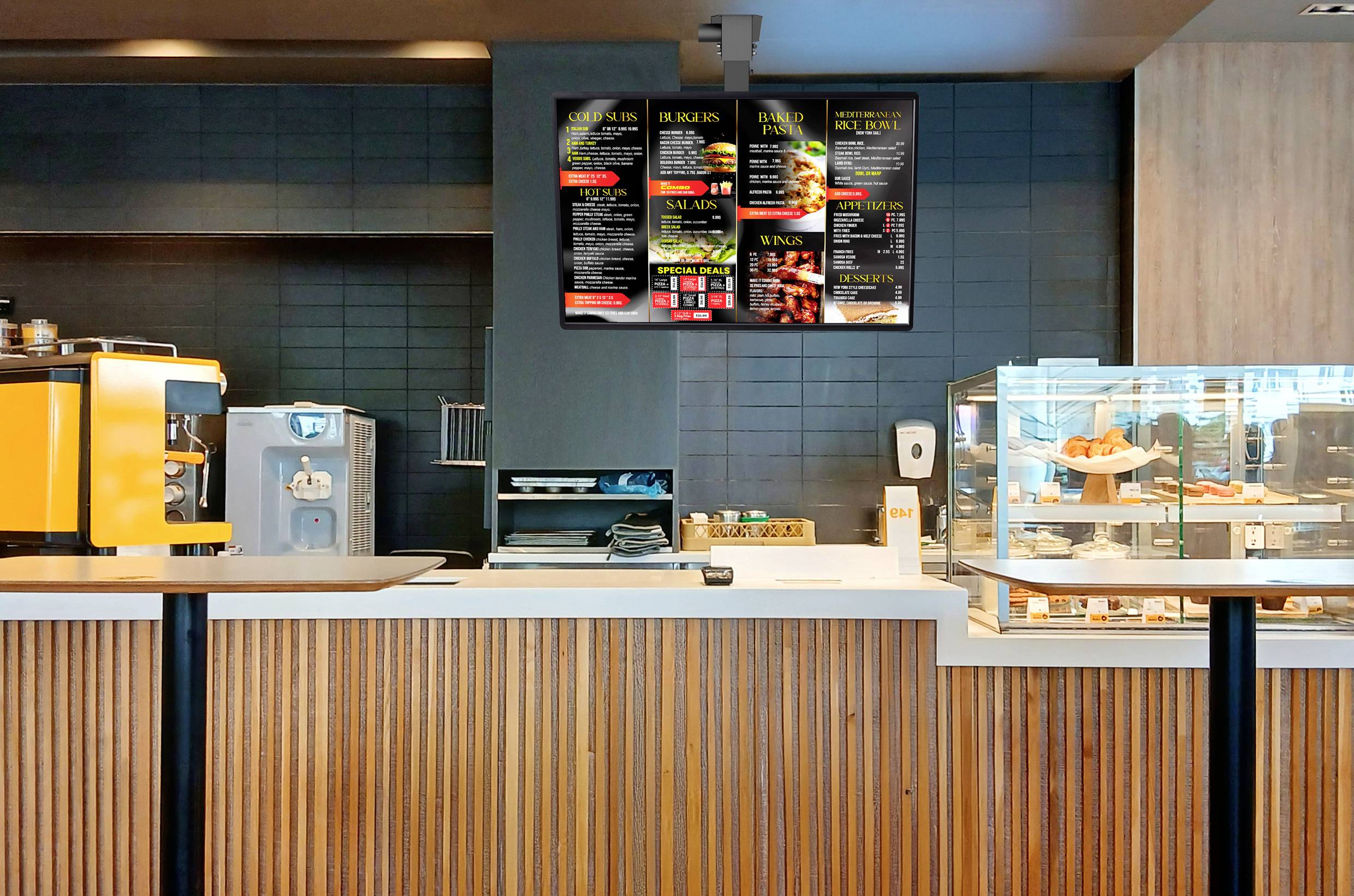 Moderní kavárový pult s proskleným výstavním pultem s pečivem, kávovarem a digitálními menu obrazovkami zavěšenými nahoře, které zobrazují různé jídlo a nápojové nabídky.