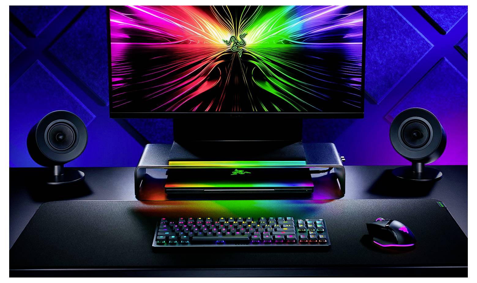 Barevné počítačové pracoviště s zářícím monitorem zobrazujícím živé digitální umění, elegantní klávesnicí, myší a dvěma reproduktory.