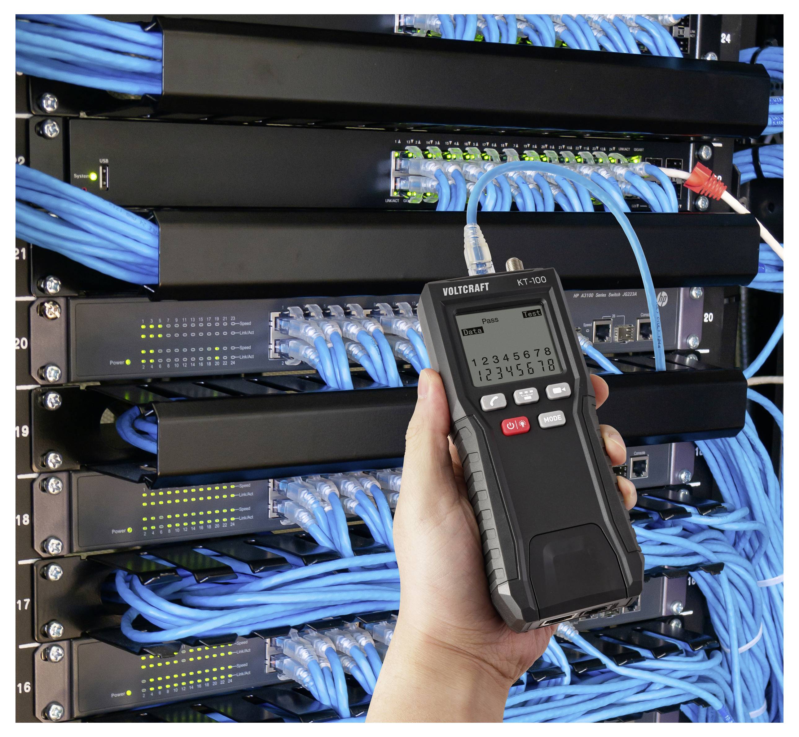 Ruka držící tester síťových kabelů před serverovou skříní plnou uspořádaných modrých kabelů a síťových switchů.