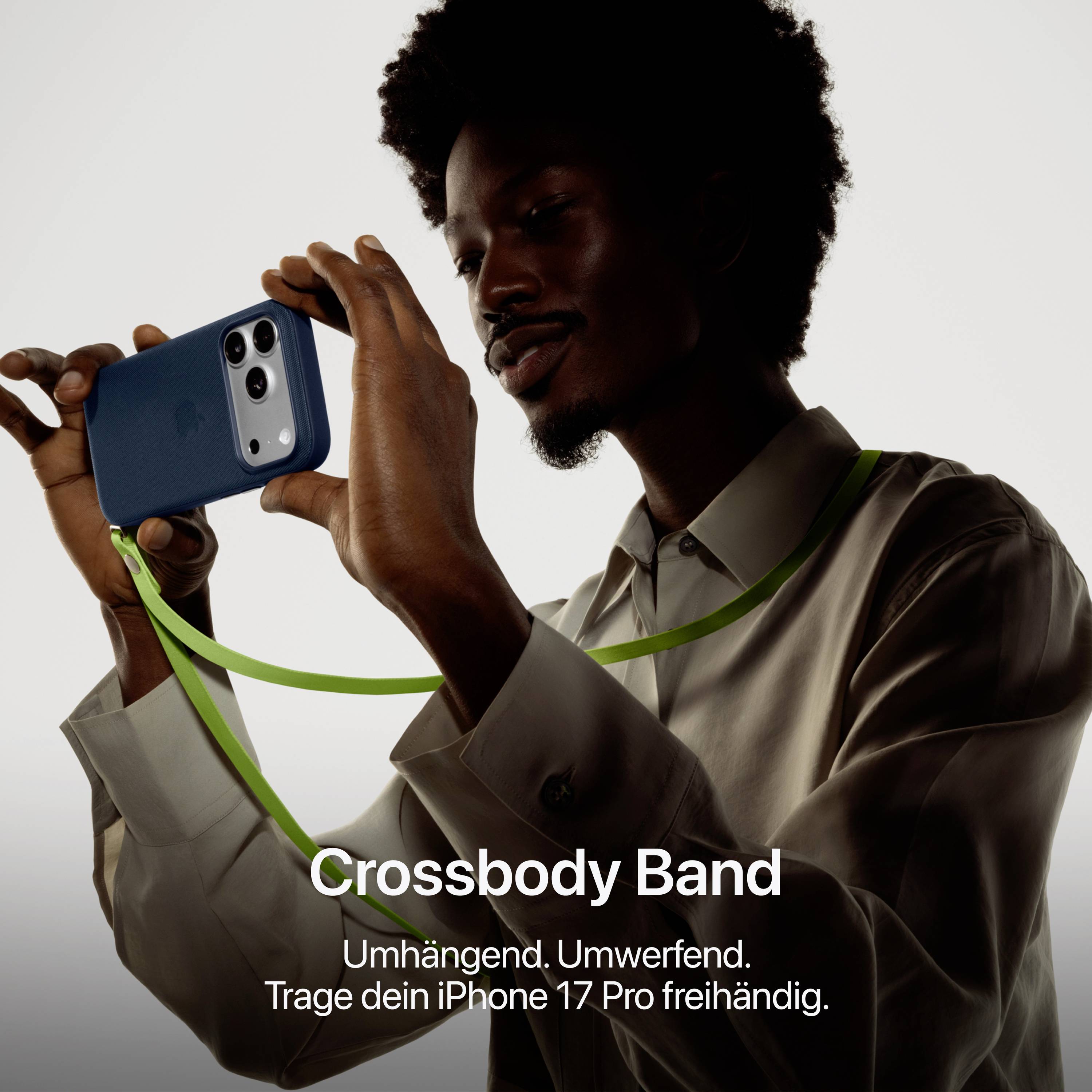 Muž drží iPhone 17 Pro s crossbody popruhem. Text: 'Crossbody popruh. Přes rameno. Okouzlující. Nos svůj iPhone 17 Pro zcela volně.'
