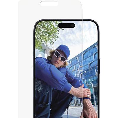 Osoba v modré bundě, čepici a slunečních brýlích dřepící venku s moderní skleněnou budovou v pozadí, odrážející se na displeji smartphonu.