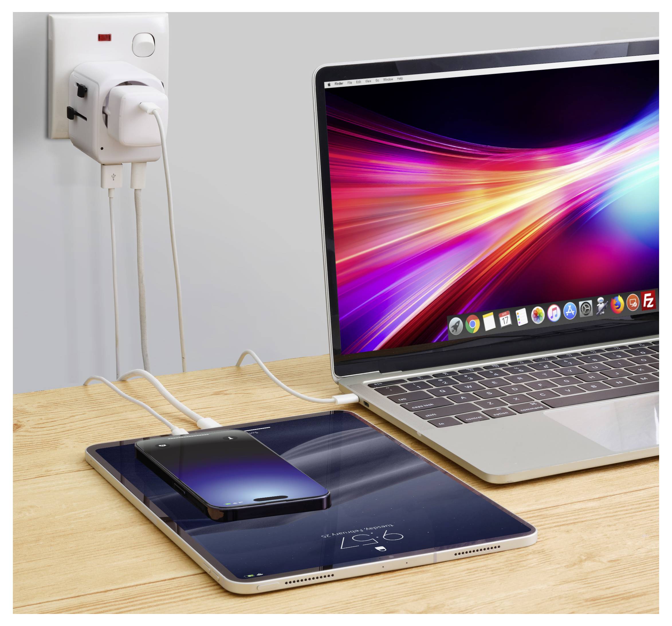 Laptop zobrazující živý displej, smartphone a tablet se nabíjejí na dřevěném stole, připojené k elektrické zásuvce.