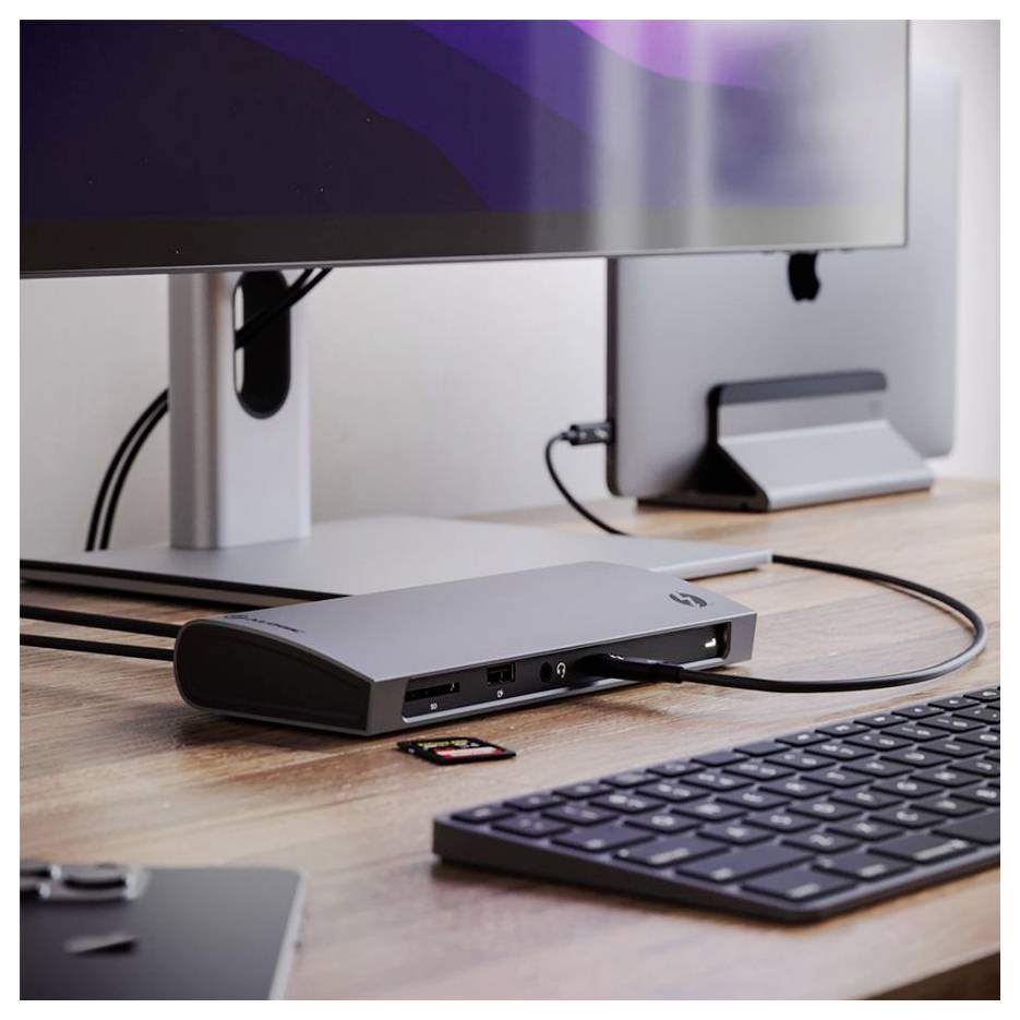 Desktopové pracoviště s monitorem, klávesnicí a dokovací stanicí připojené dohromady. Malé zařízení je umístěno vedle klávesnice na dřevěném stole.
