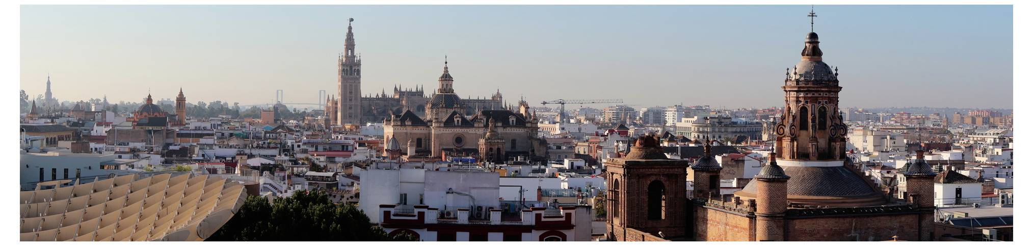 Panoramatický pohled na Sevillu ve Španělsku, zobrazující ikonické památky jako Giraldovu věž a Metropol Parasol na pozadí jasné oblohy.
