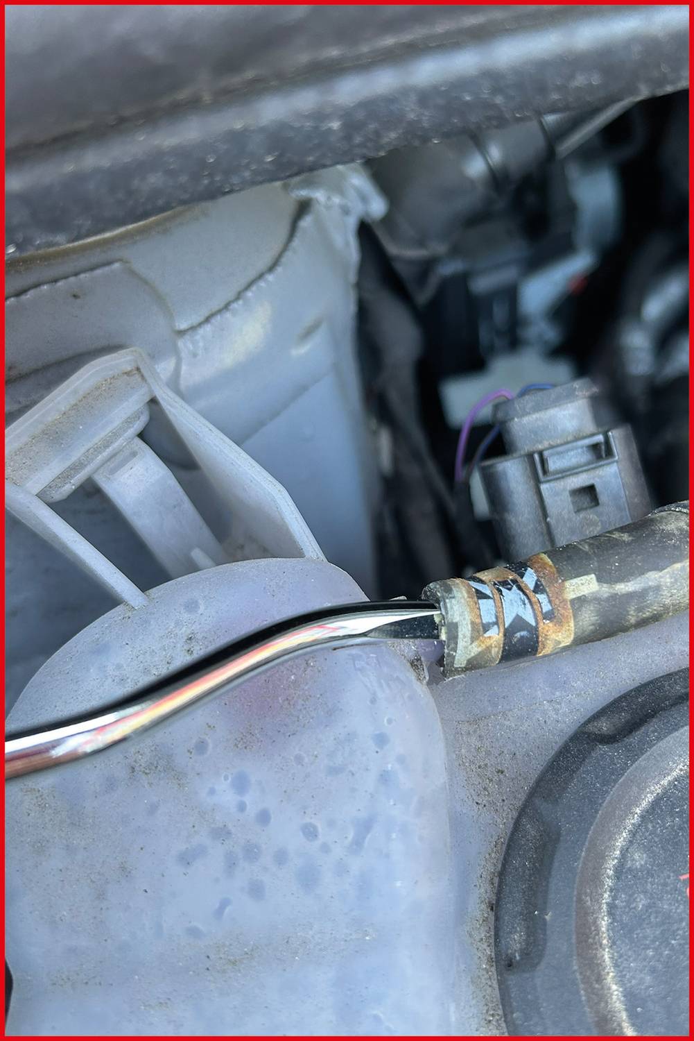 Detailní záběr komponenty automobilového motoru zobrazující připojený vodič a plastovou část, což naznačuje kontext údržby nebo opravy.