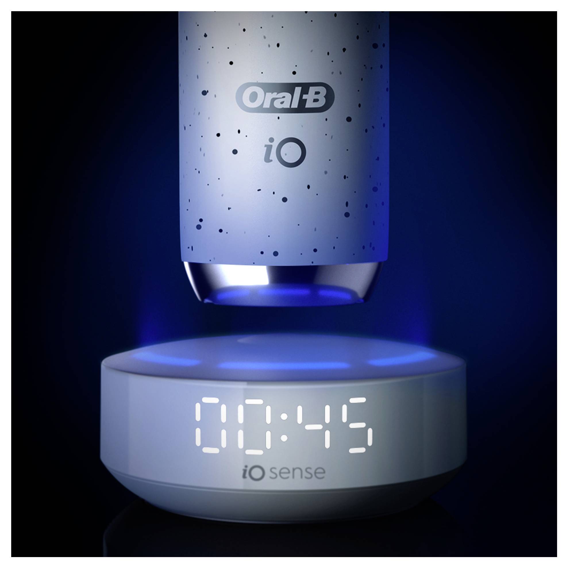 Elektrická zubní kartáček nad nabíjecí stanicí zobrazující '00:45' s modrým osvětlením; označený značkou 'Oral-B iO' a 'iO Sense'.