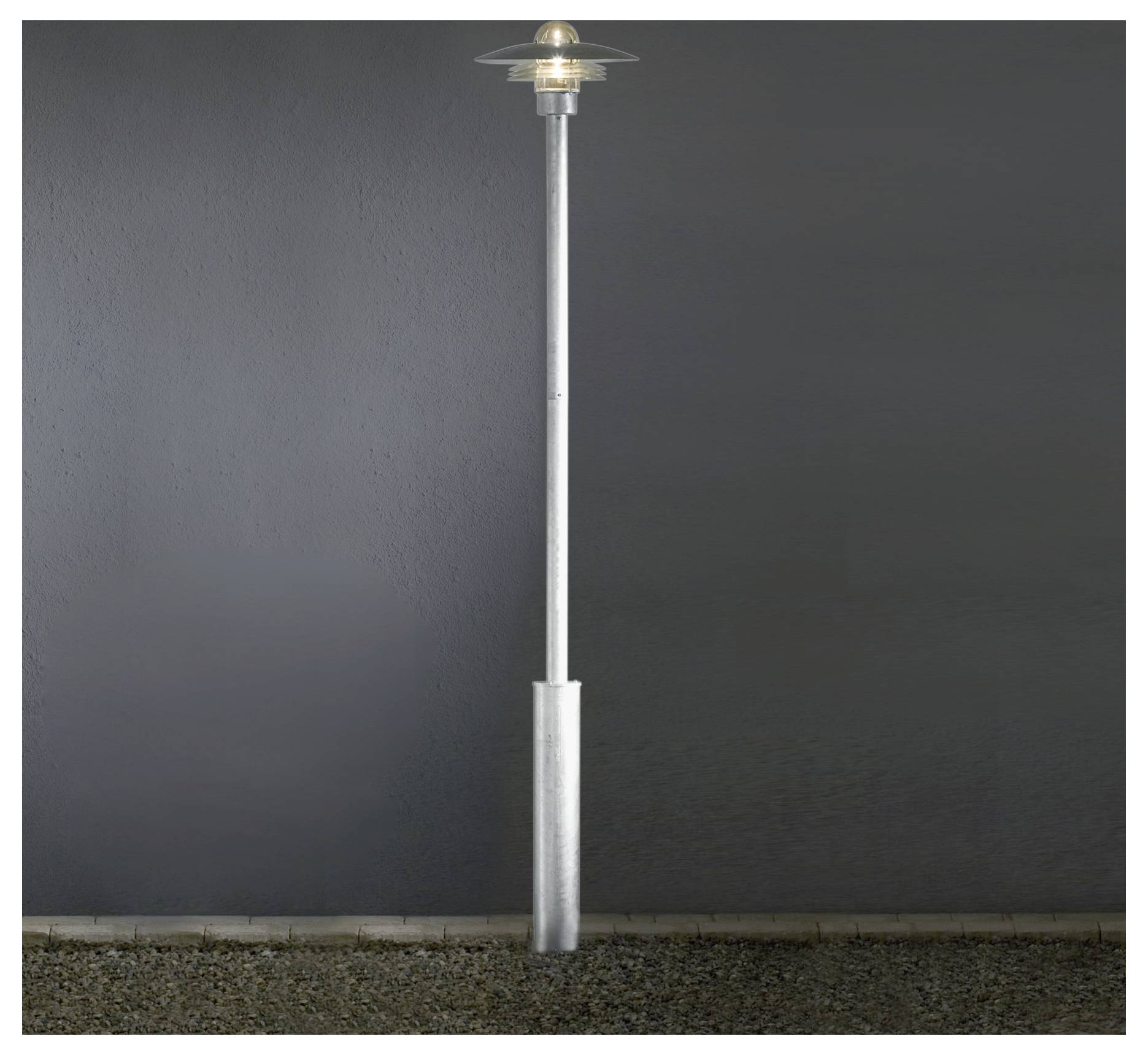 Vysoká kovová pouliční lampa s kruhovým světelným tělesem je umístěna proti jednoduché tmavé pozadí, osvětlující své okolí.