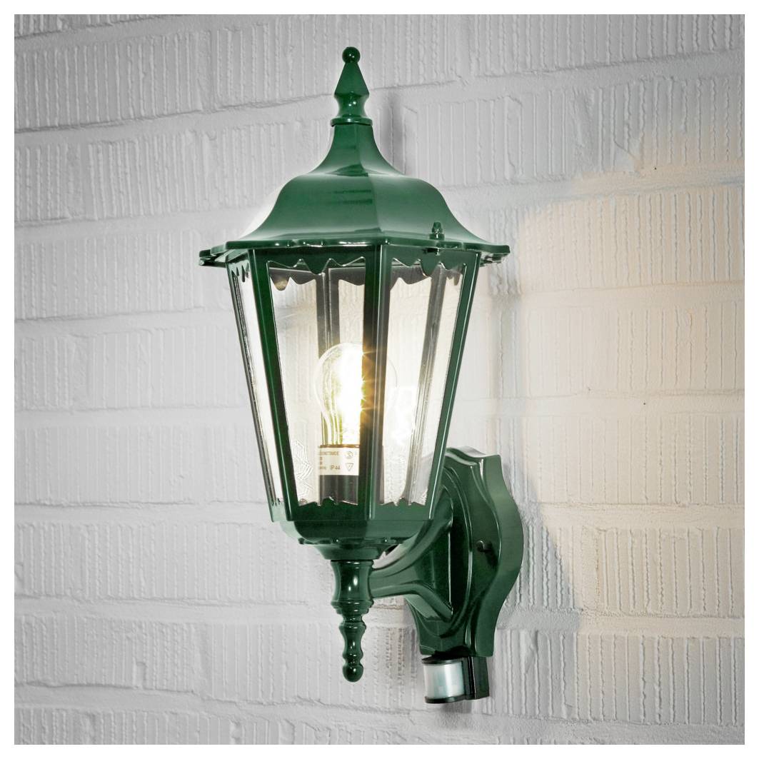 Dobová nástěnná lampa v zelené barvě s viditelnou žárovkou osvětluje bílou cihlovou zeď a vytváří klasickou a elegantní venkovní atmosféru.