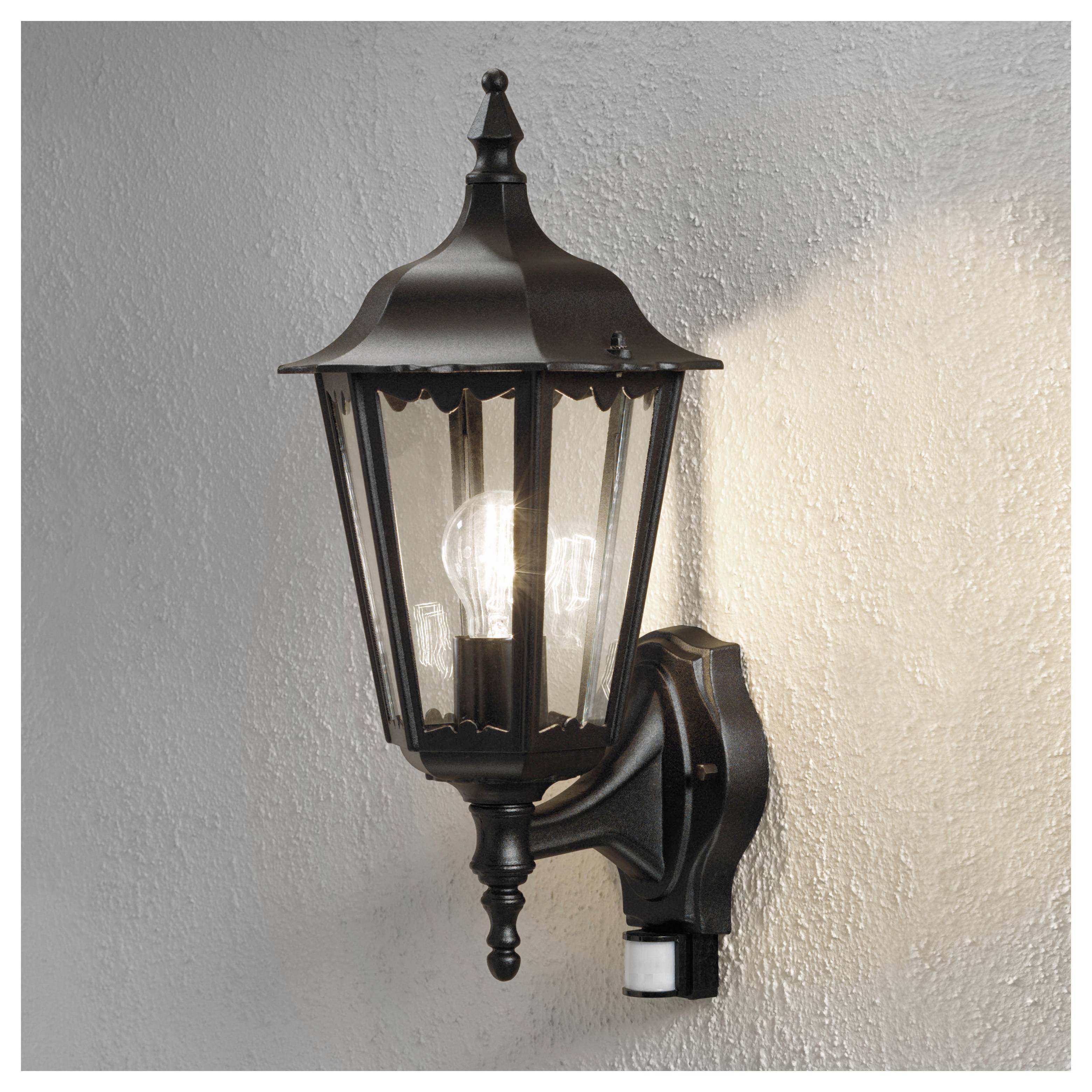 Černá, vintage lampa připevněná na zdi, uvnitř s žhnoucí žárovkou, osvětlující okolní texturovaný povrch.