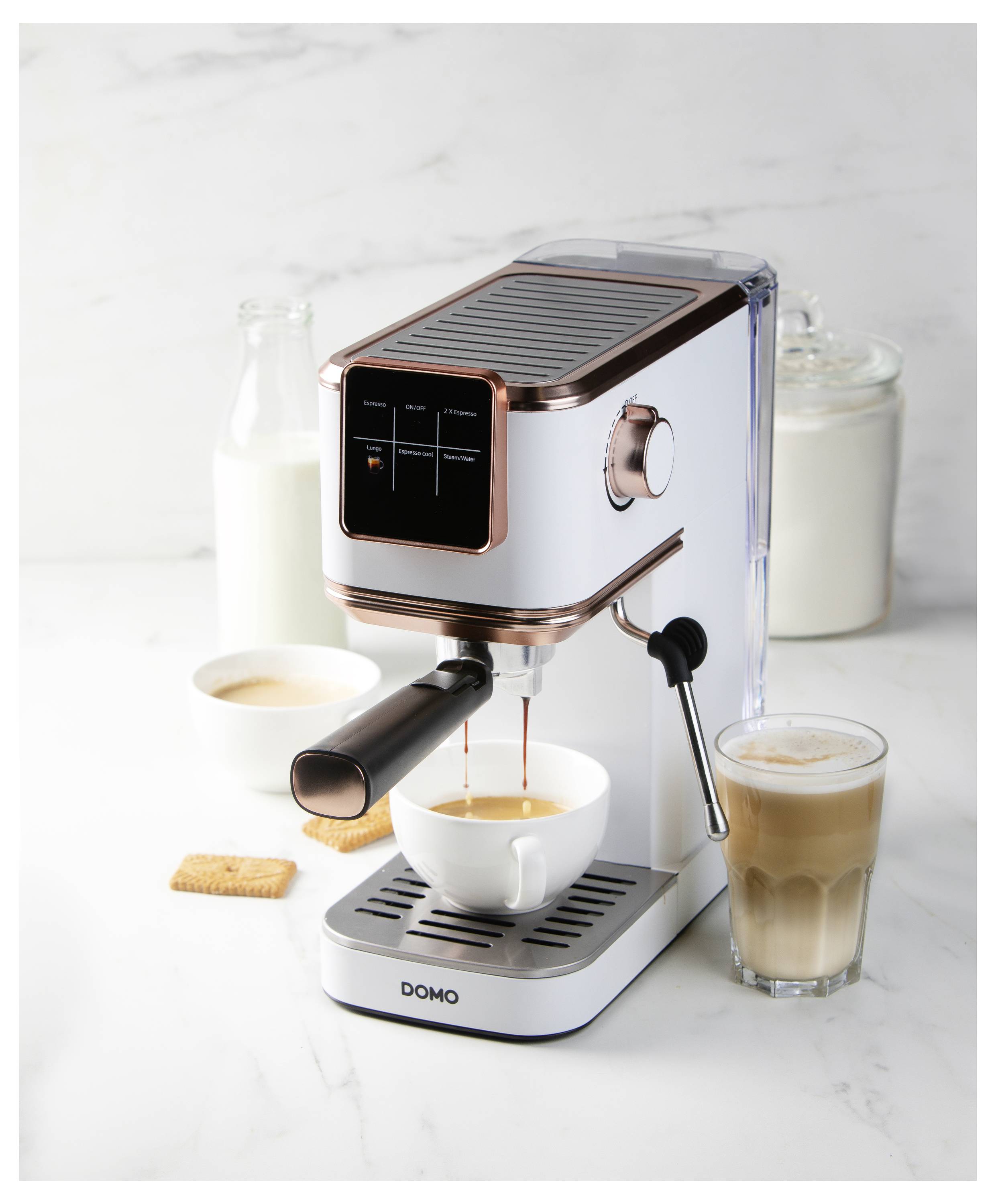 Domácí espresso kávovar připravující kávu do šálku, s mlékem a cukrem poblíž, sklenicí latté na straně a sušenkou v pozadí.