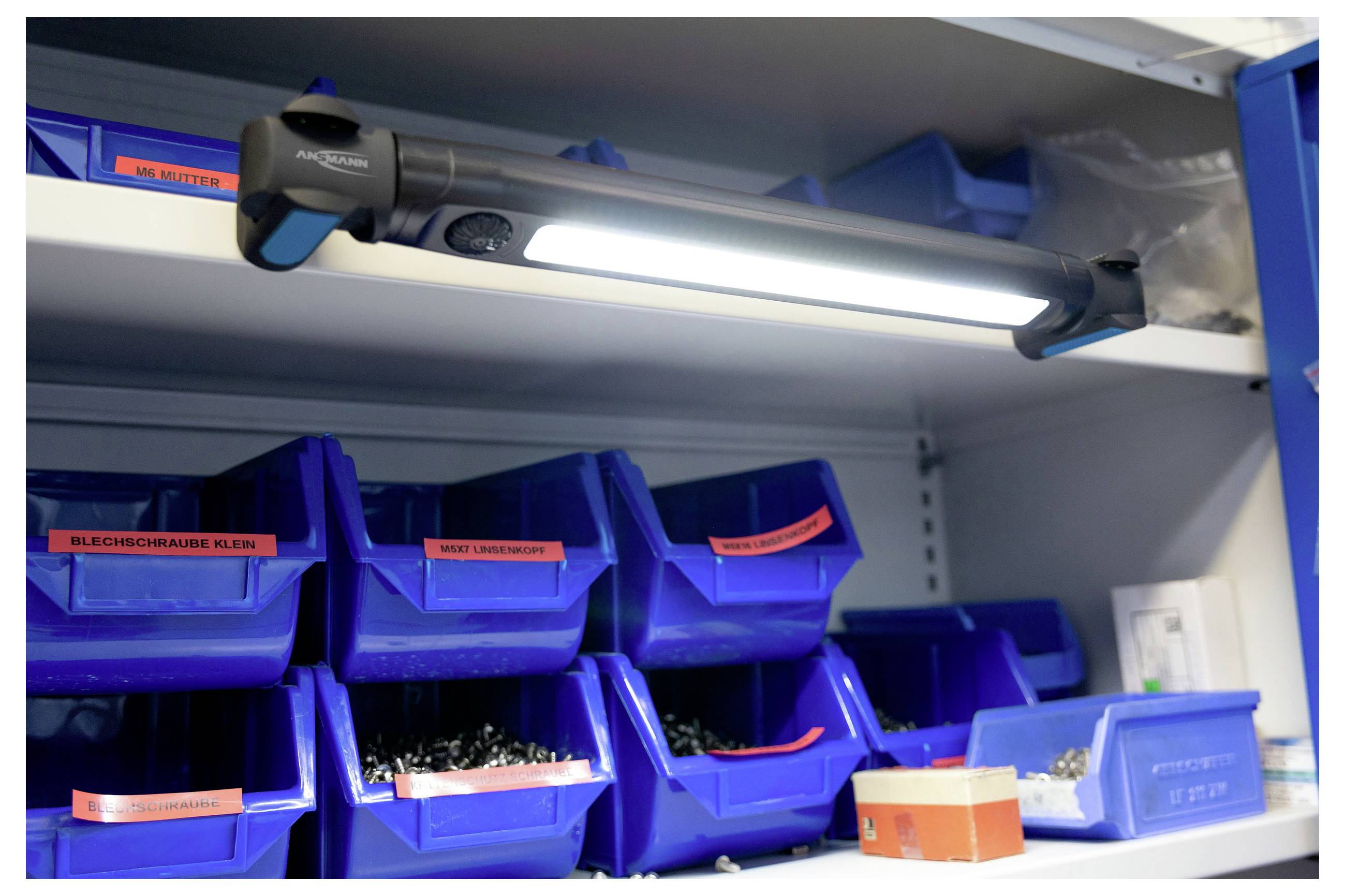 LED pracovní světlo připevněné pod policí, osvětlující modré boxy naplněné různými šrouby a hardwarovými komponenty na policích.