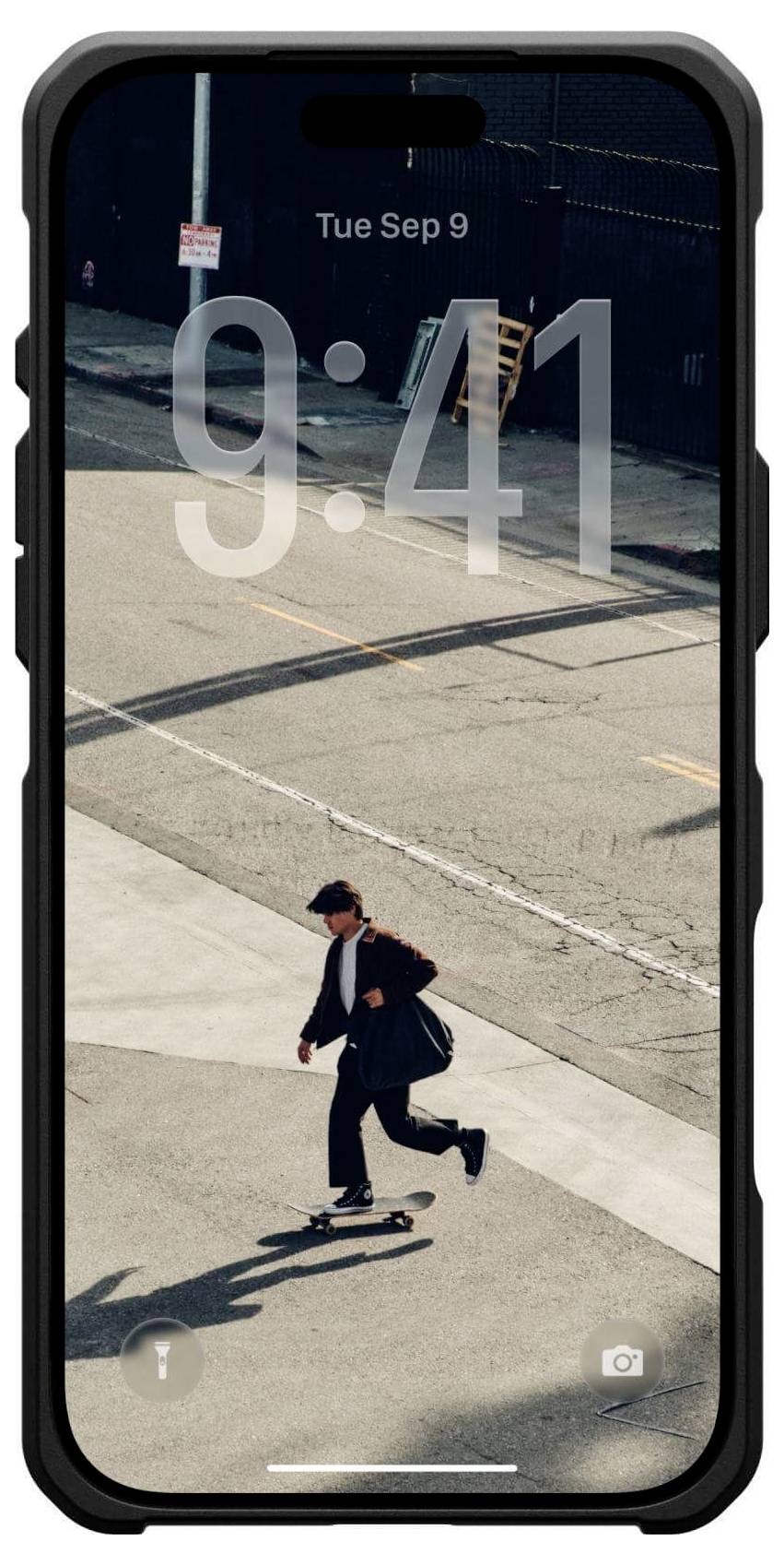 Osoba jezdí na skateboardu po městské ulici v obleku a s taškou přes rameno. Na zamčené obrazovce telefonu je čas '9:41'.