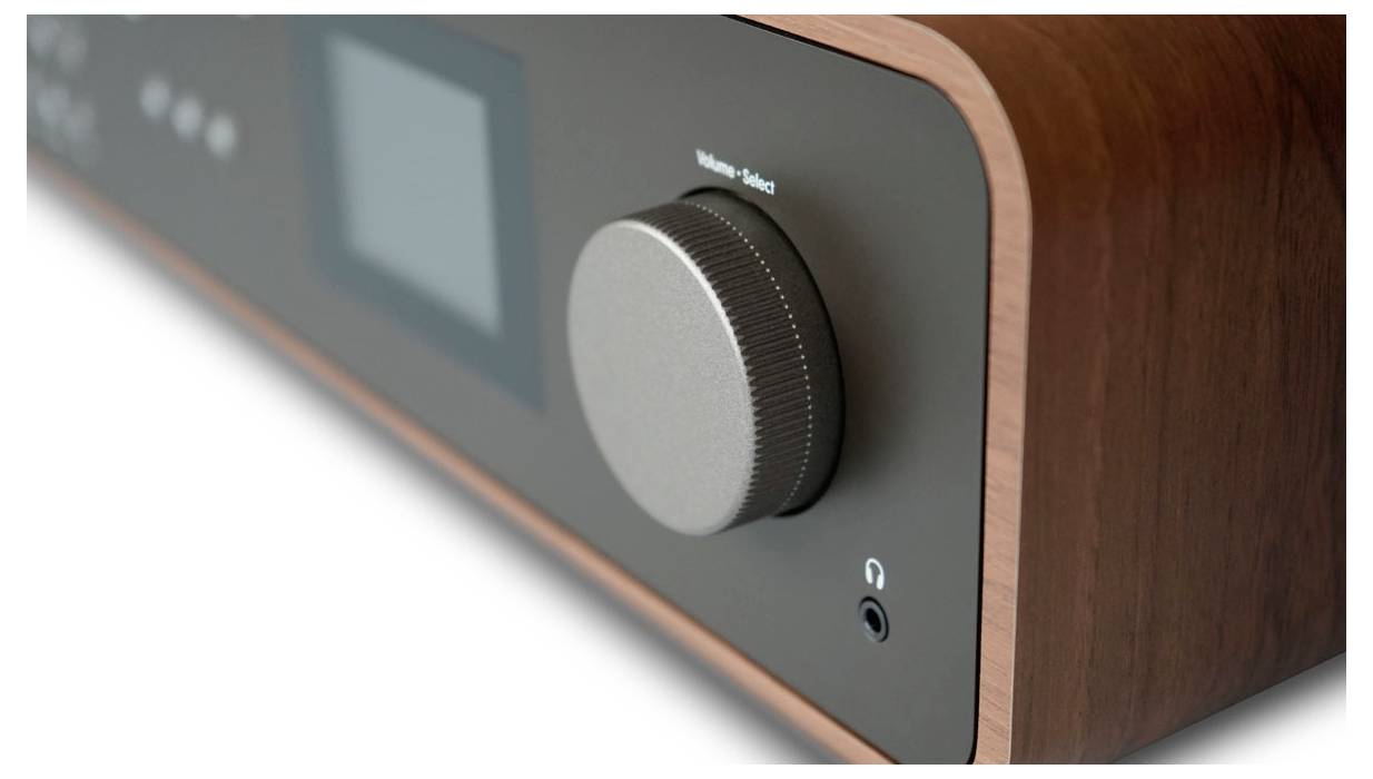 Detailní záběr vintage audiopřístroje s velkým ovládacím knoflíkem a zdířkou pro sluchátka na dřevěném a tmavém panelu.