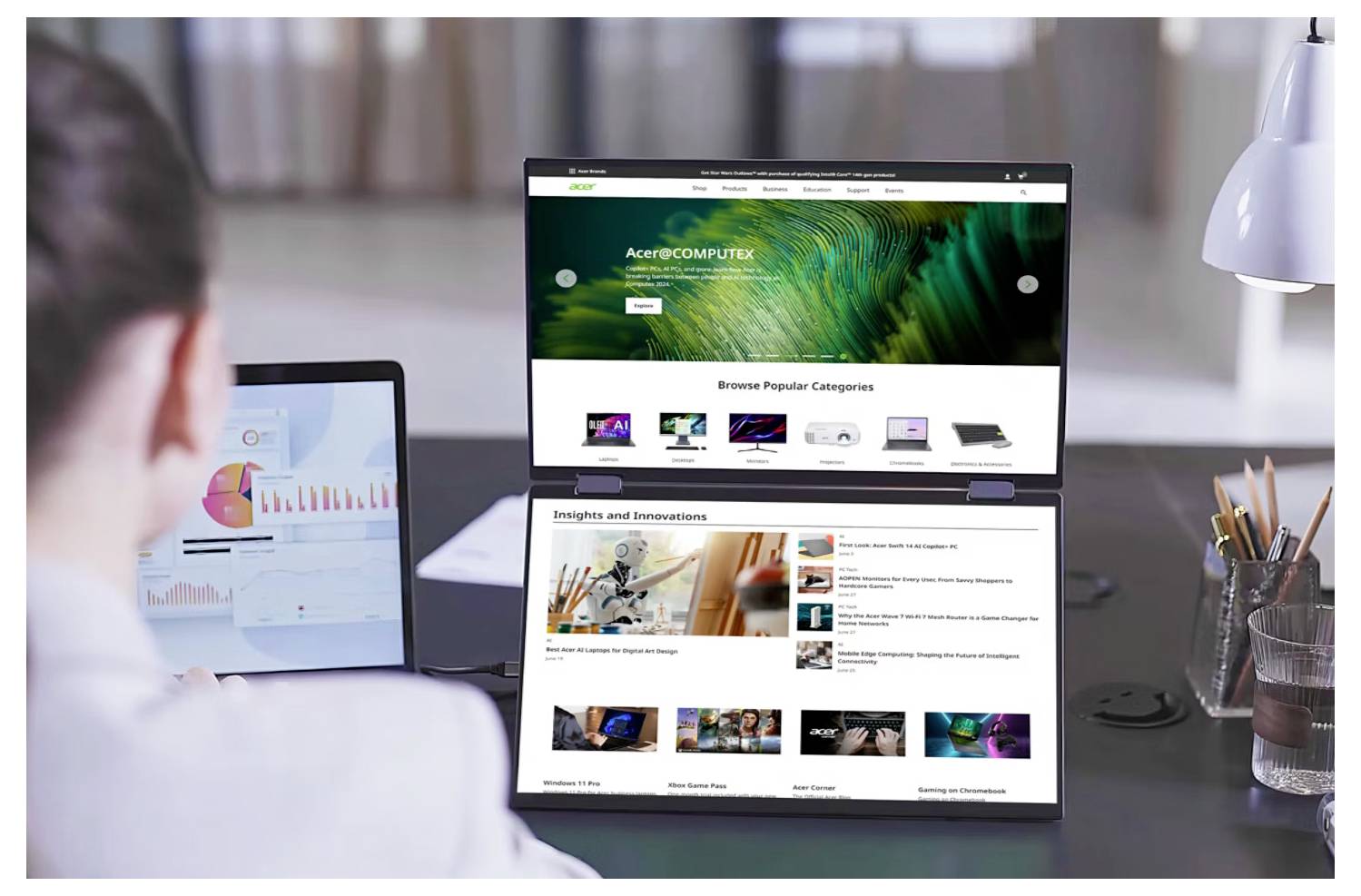 Osoba pracuje u stolu na notebooku s duálním displejem, kde první obrazovka zobrazuje homepage technologického webu. Druhá obrazovka prezentuje barevný datový graf.