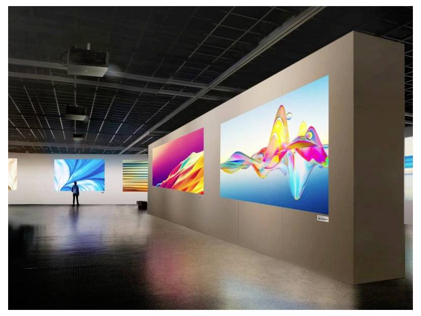 Umělecká galerie vystavující velké, barevné abstraktní digitální umělecké dílo na stěnách. Osoba stojí a prohlíží si jeden z exponátů.