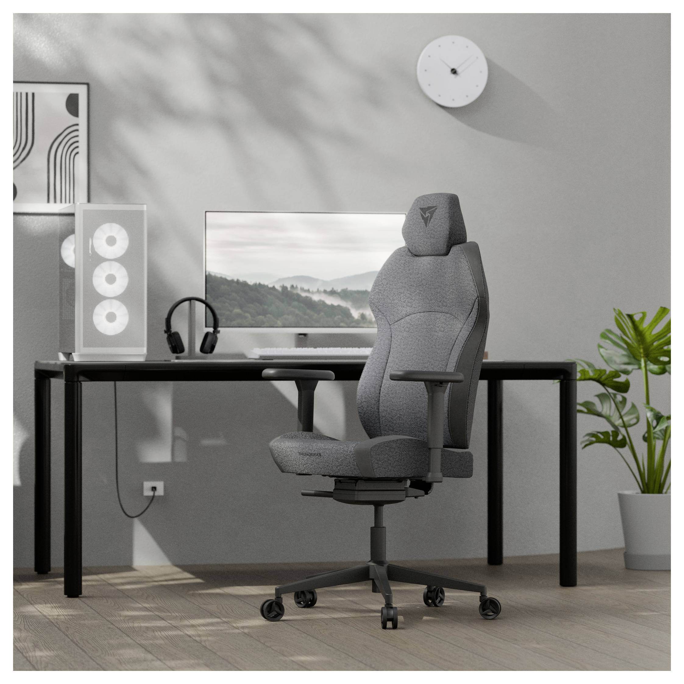 Moderní domácí kancelář s šedou ergonomickou židlí, černým stolem, velkým monitorem, pokojovou rostlinou, nástěnným hodinami a minimalistickým dekorem.