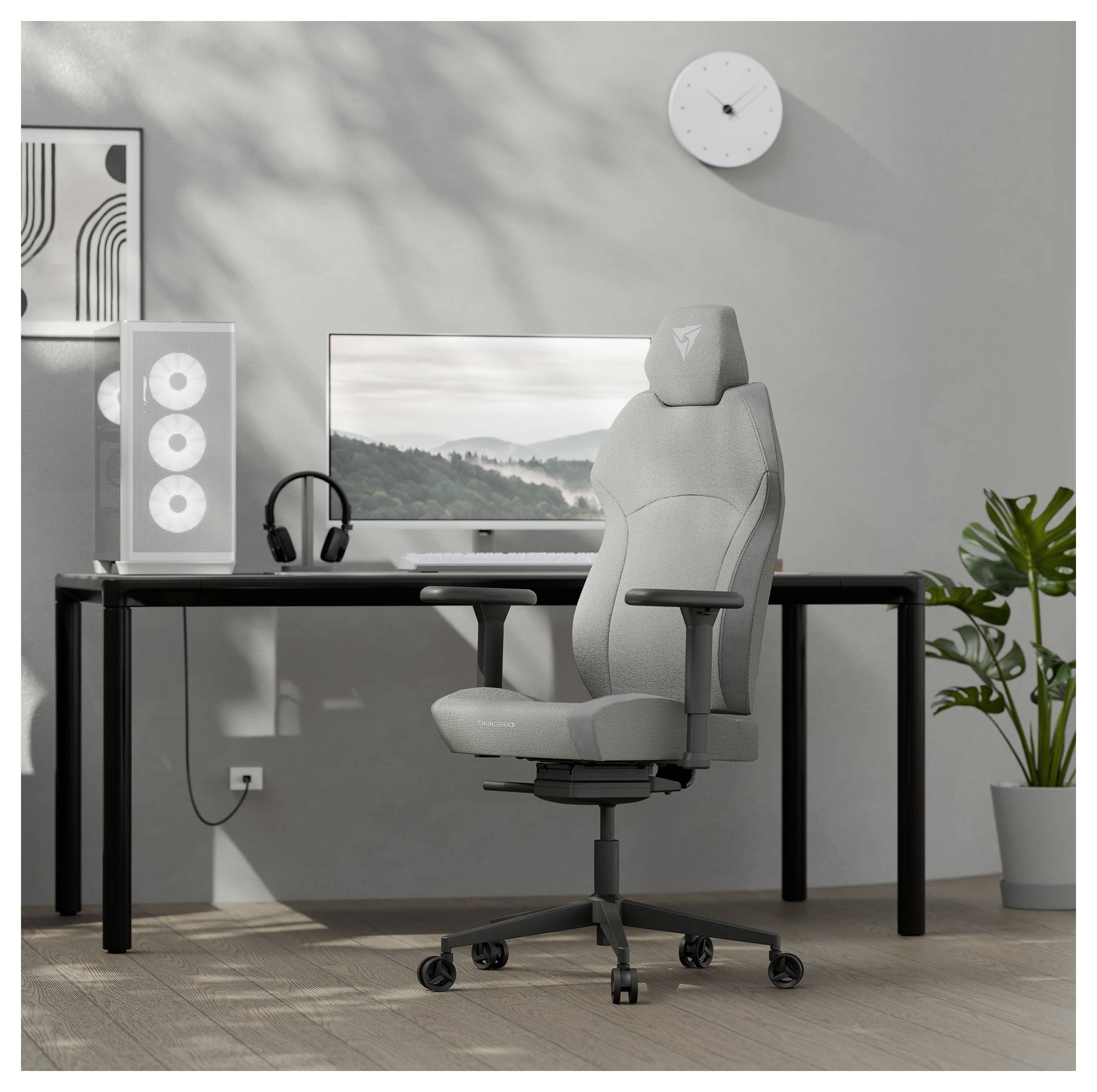Moderní domácí pracovna s elegantním stolem, počítačovým monitorem, herní židlí, headsetem a vysokou rostlinou, vše v neutrálních tónech.