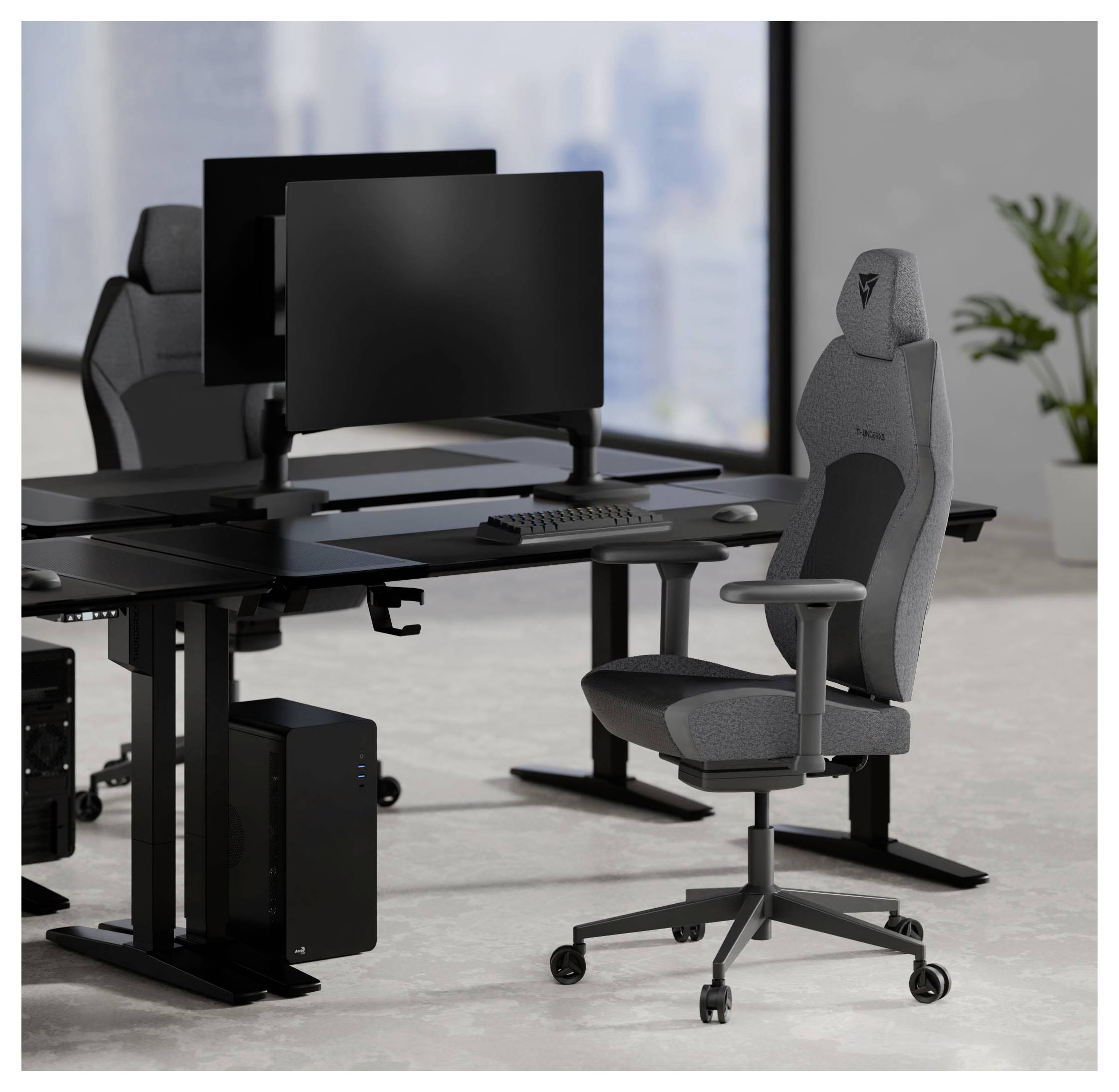 Moderní kancelářské pracoviště se dvěma ergonomickými židlemi a dvěma monitory na nastavitelných stolech, umístěné proti panoramatickému výhledu na městskou krajinu.