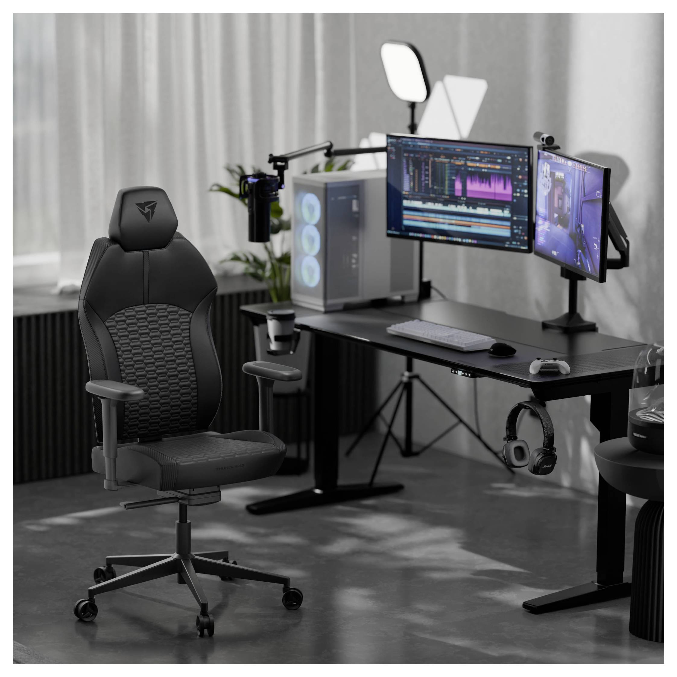 Herní sestava s duálními monitory zobrazujícími audio editační software, stolní počítač, kruhové světlo, mikrofon a herní židli.