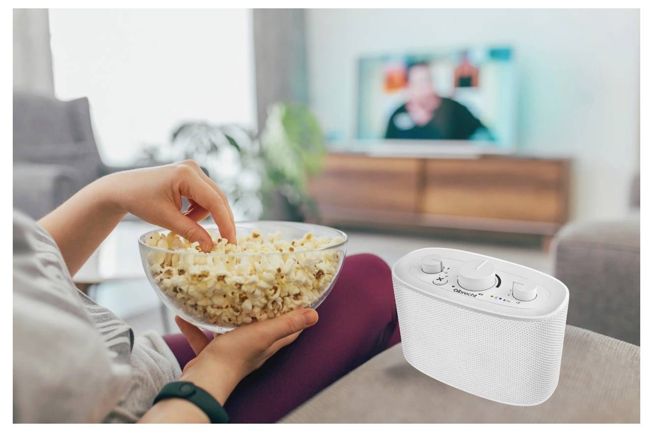 Osoba sedí na gauči a drží mísu s popcornem před televizí. Na obrazovce je zobrazený telefon se zvětšeným zvukem, což naznačuje zesílený zvuk pro sledování.