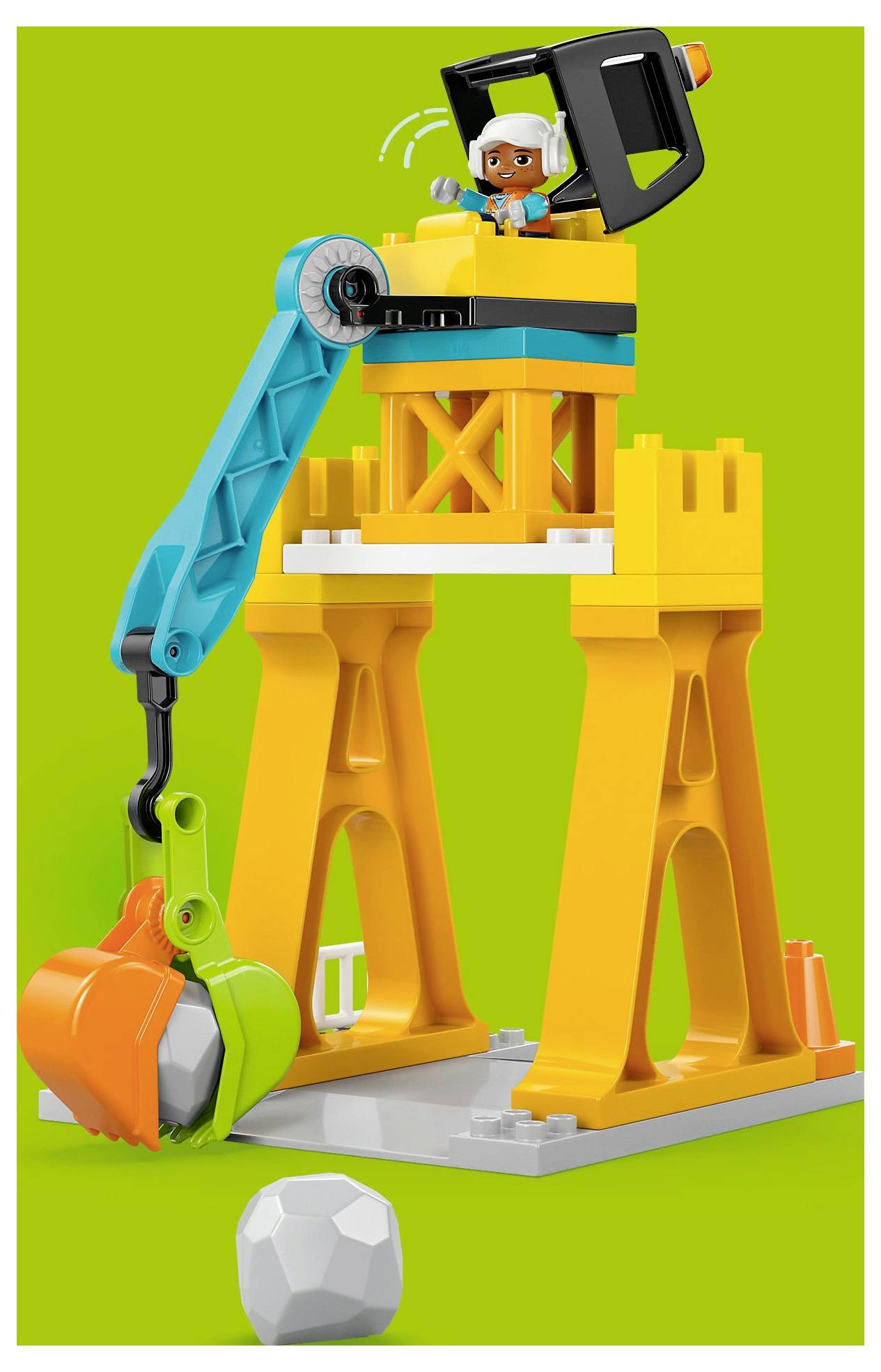 Barevný hračkářský jeřáb složený z oranžových, modrých a zelených dílů s figurkou obsluhy, umístěný na zeleném pozadí.