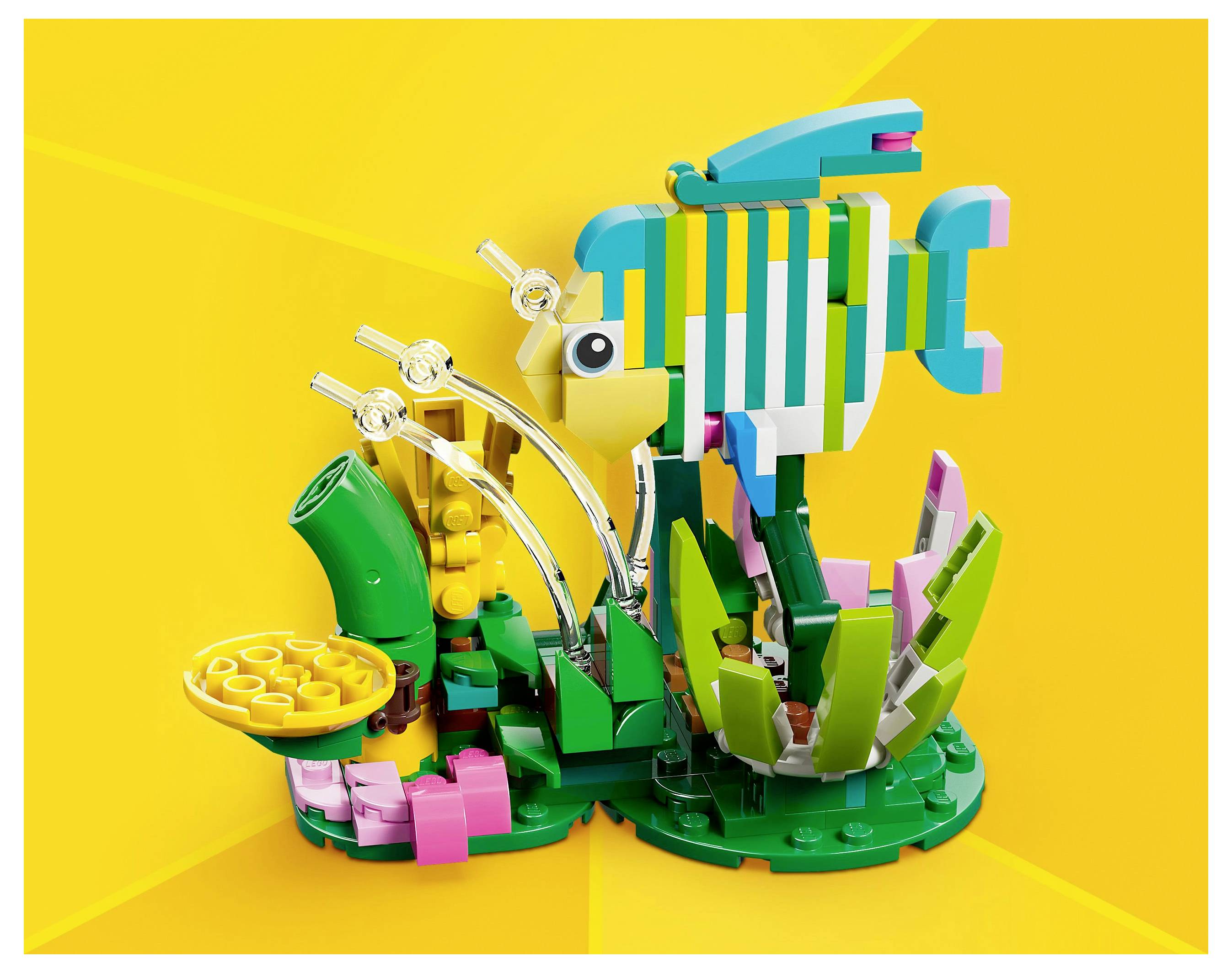 Barevná LEGO rybí expozice s výrazným žlutým pozadím, zobrazující rybu mezi zelenými a růžovými LEGO rostlinami a dekorativními prvky.