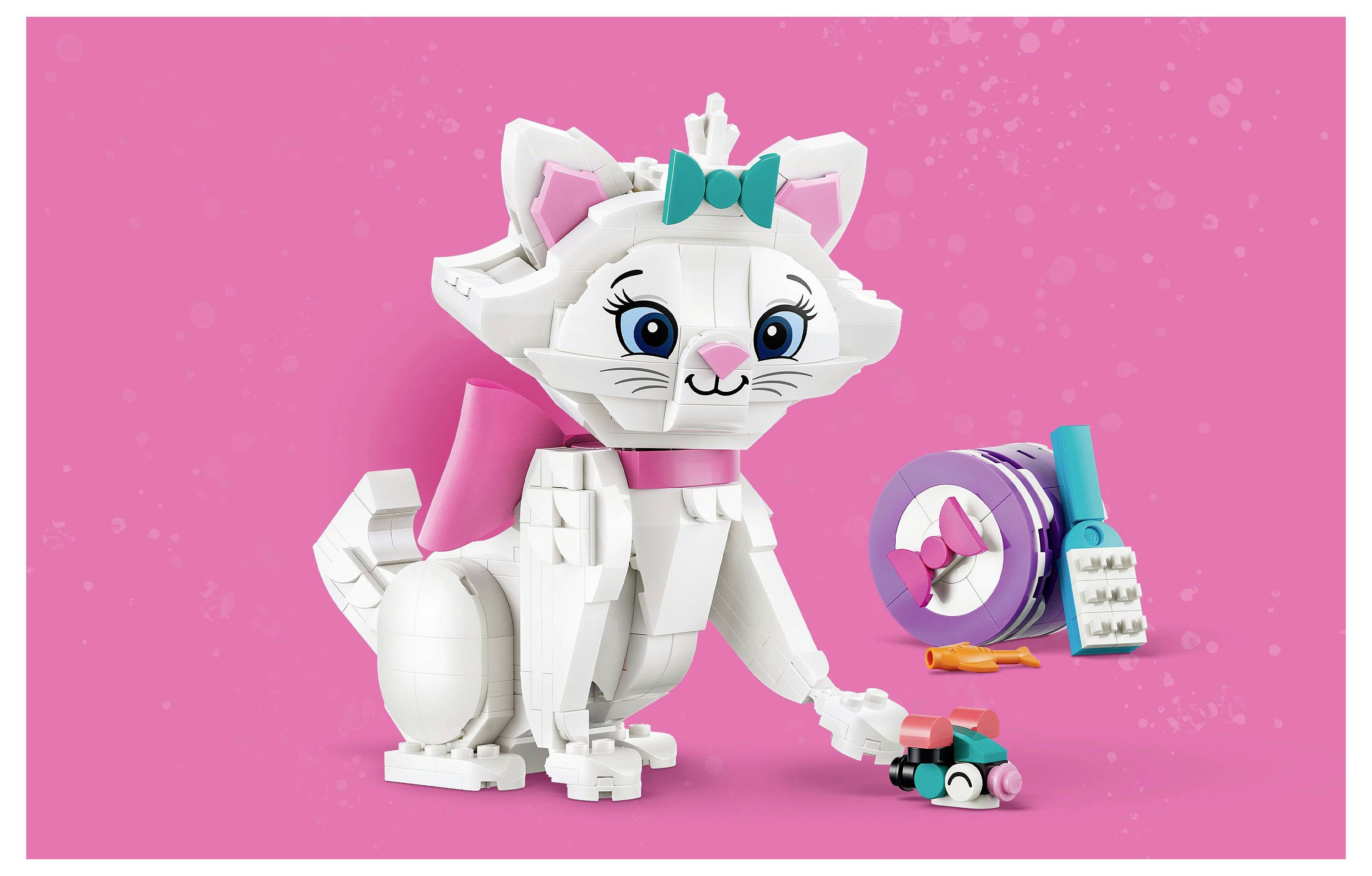Hravá hračka kočičky složená z stavebnicových kostek, s mašlí a tlačící malé autíčko, s barevnými doplňky v pozadí.
