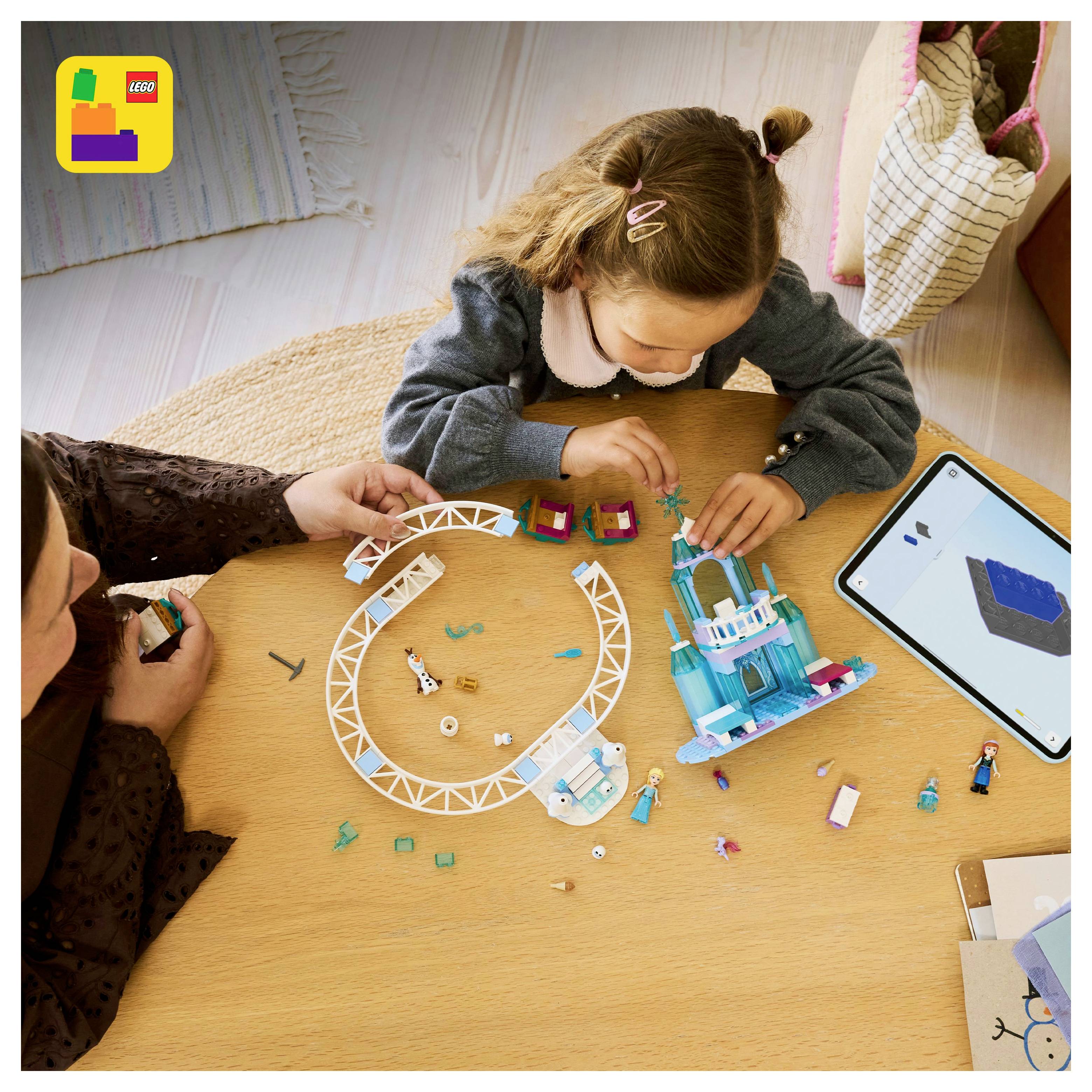 Dítě a dospělý spolupracují na stavbě LEGO sady u stolu, poblíž je tablet s návodem.