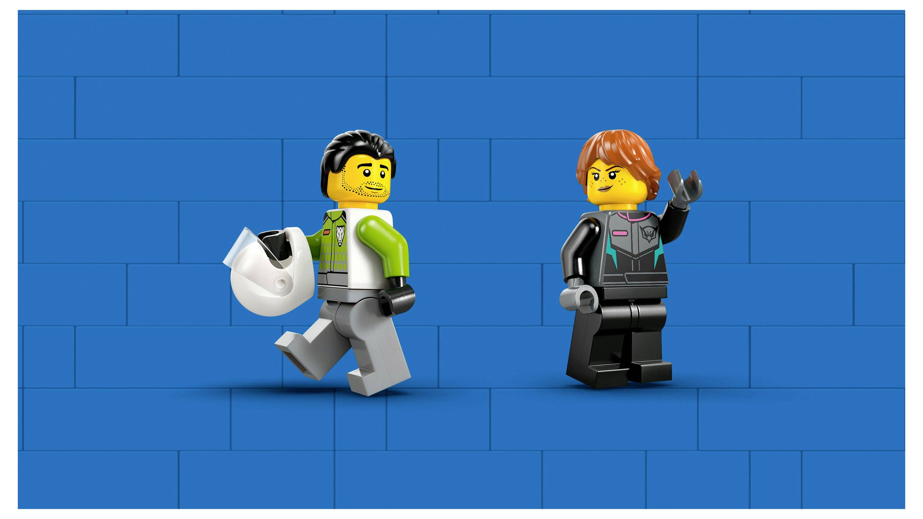 Dvě figurky LEGO na modrém cihlové pozadí: jedna drží helmu a vesele kráčí; druhá mává, oblečená v podobném oblečení.
