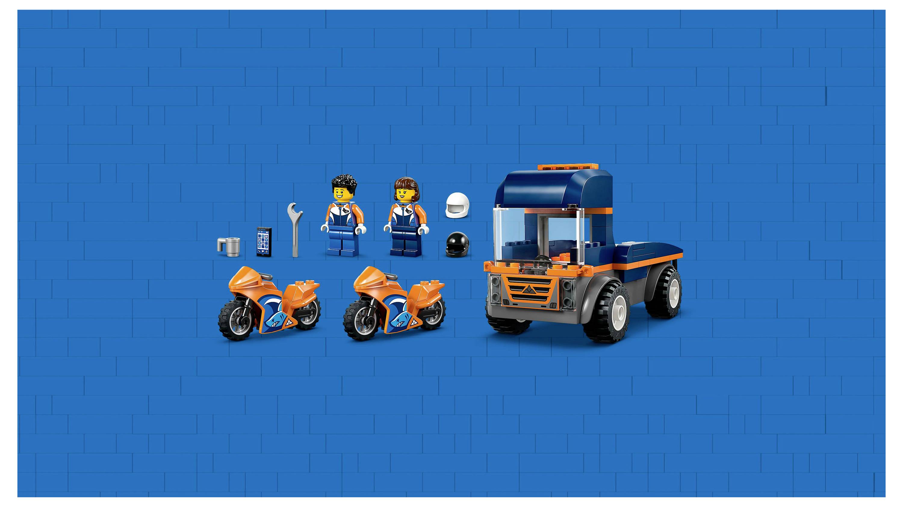 Dvě hračkářské figurky v modrém a oranžovém oblečení, dvě oranžové motorky a modrý náklaďák na modrém pozadí. Příslušenství zahrnuje helmy a nástroje.