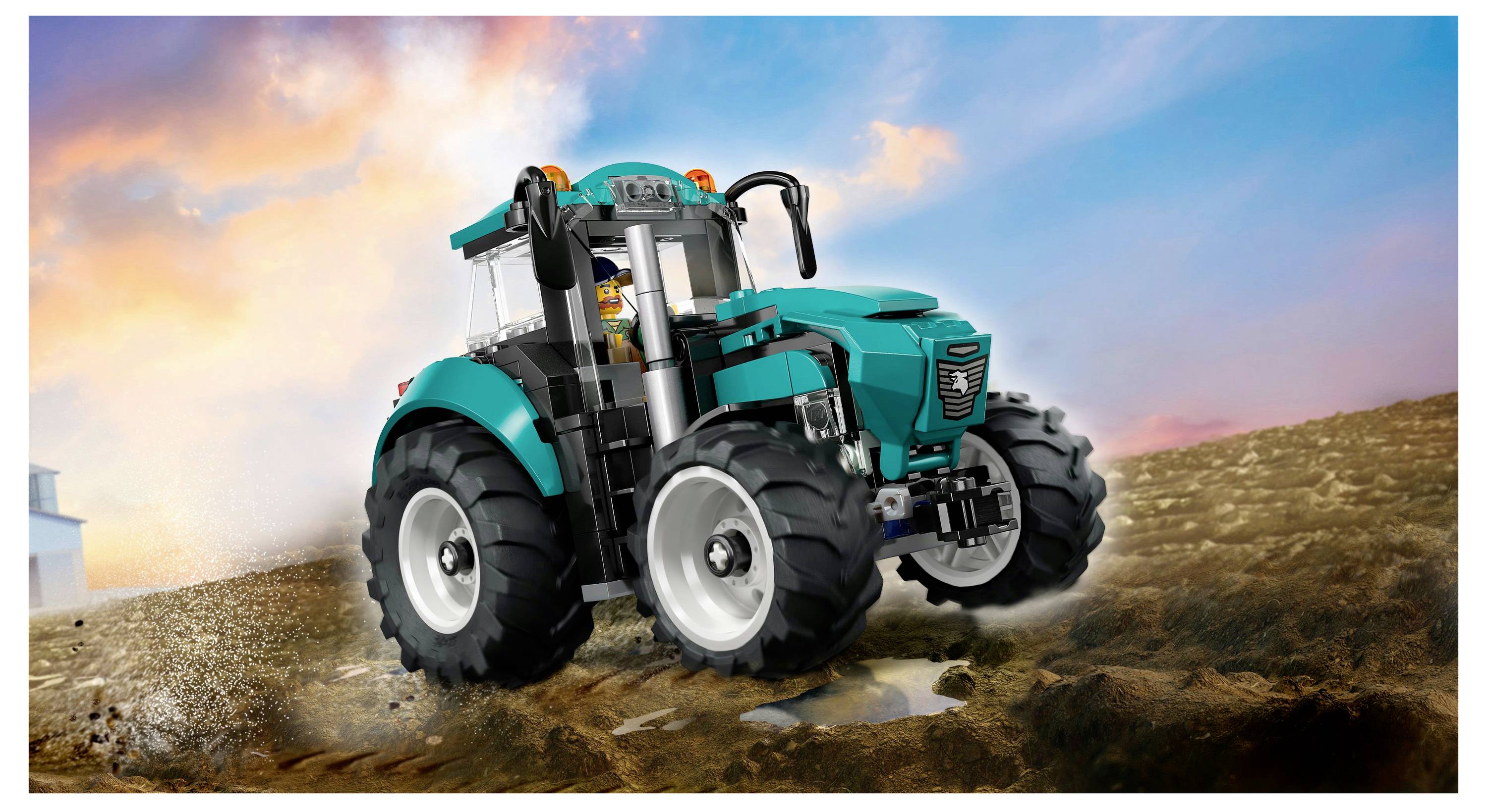 Hračkářský traktor s velkými koly a figurkou farmáře stojí na prašné cestě před barevným nebem.